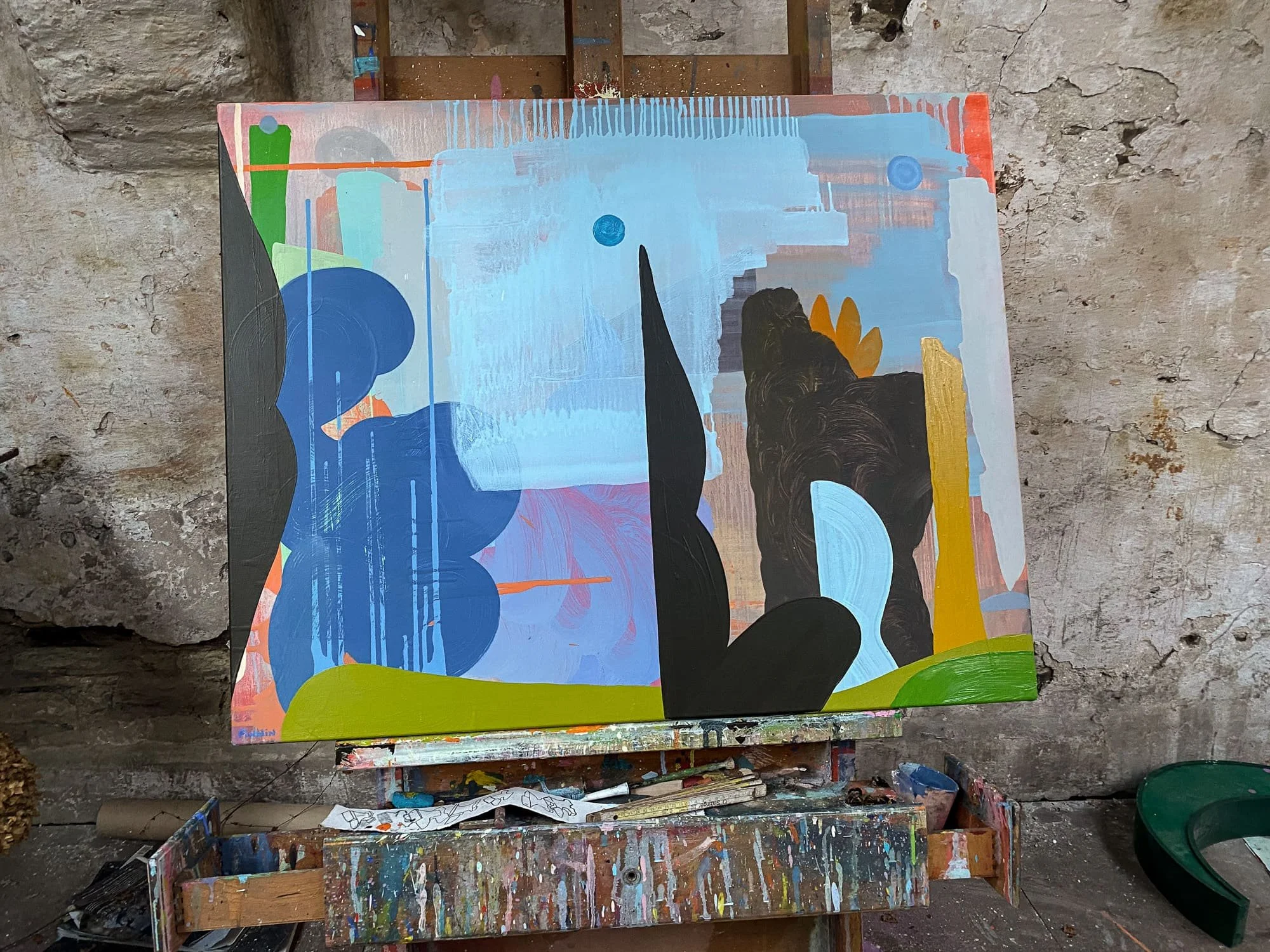 Abstract oil painting on easel in artist studio, blue black and olive green canvas with dark sculptural forms, finished painting resting on paint-covered easle, Martin Finnin Irish artist