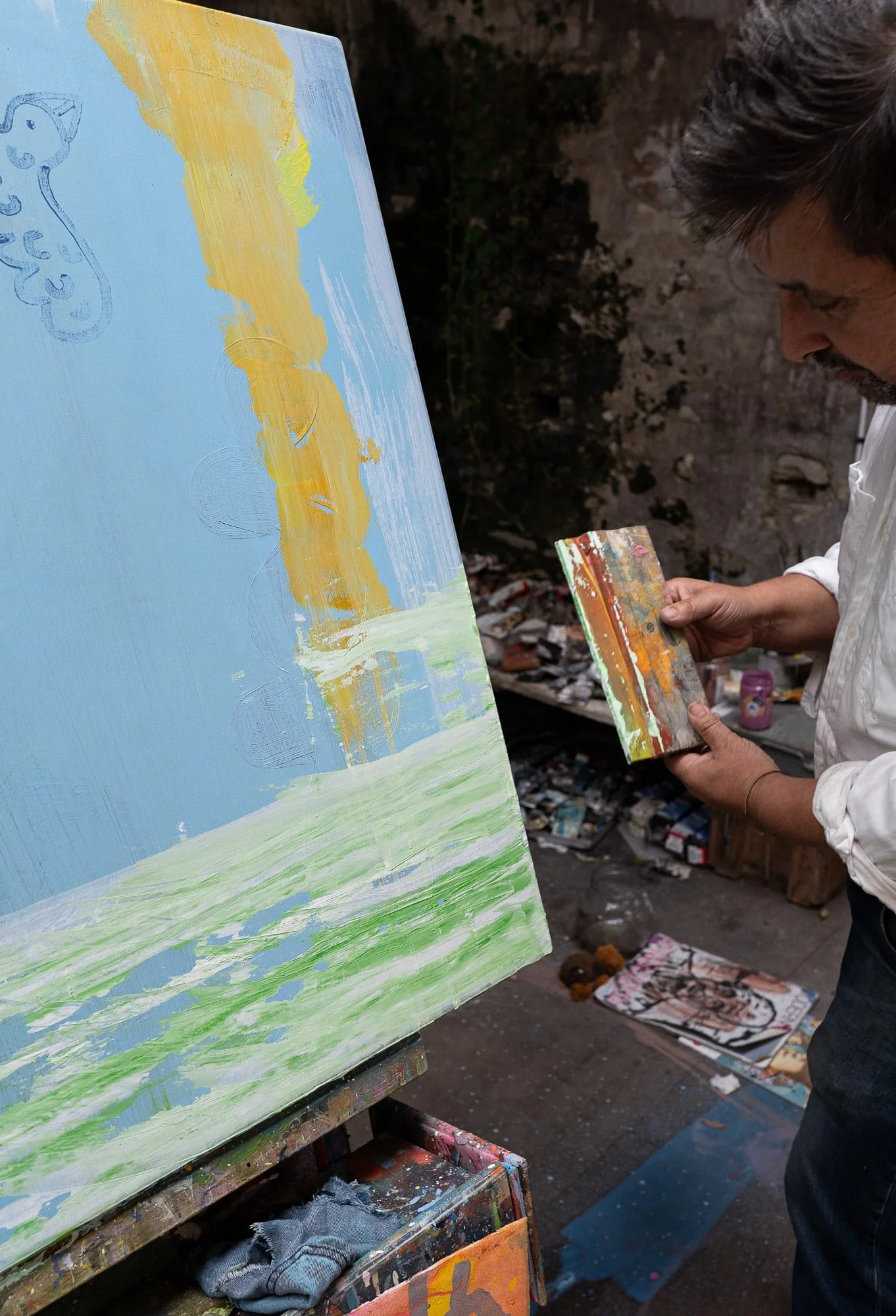 Irish artist Martin Finnin applying oil paint to blue canvas with squeegee in West Cork studio, mint green sky forming, abstract painting in progress on easel