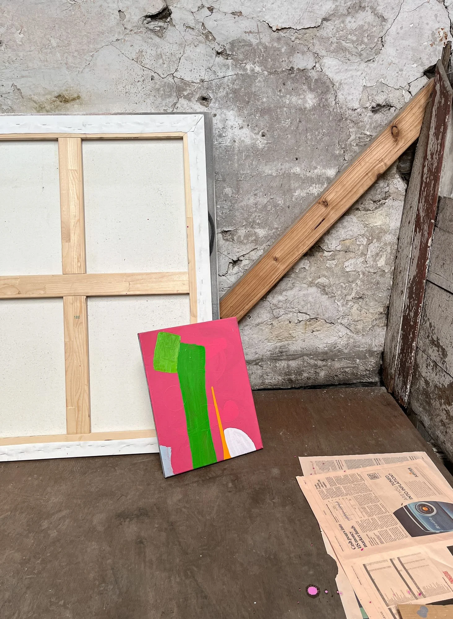 Small abstract oil painting in progress leaning against stone wall in West Cork studio, vivid green and orange forms on pink ground, blank canvas and newspaper beside it, Martin Finnin Irish artist