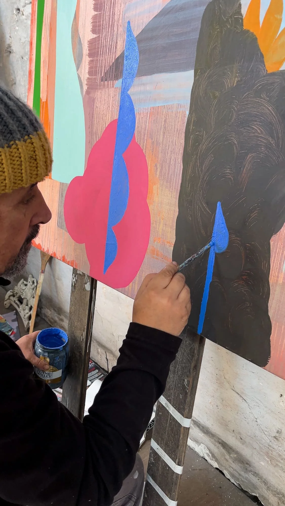 Irish artist Martin Finnin painting bold blue form onto large abstract canvas, vivid pink and dark black forms in progress, close up of artist working in West Cork studio