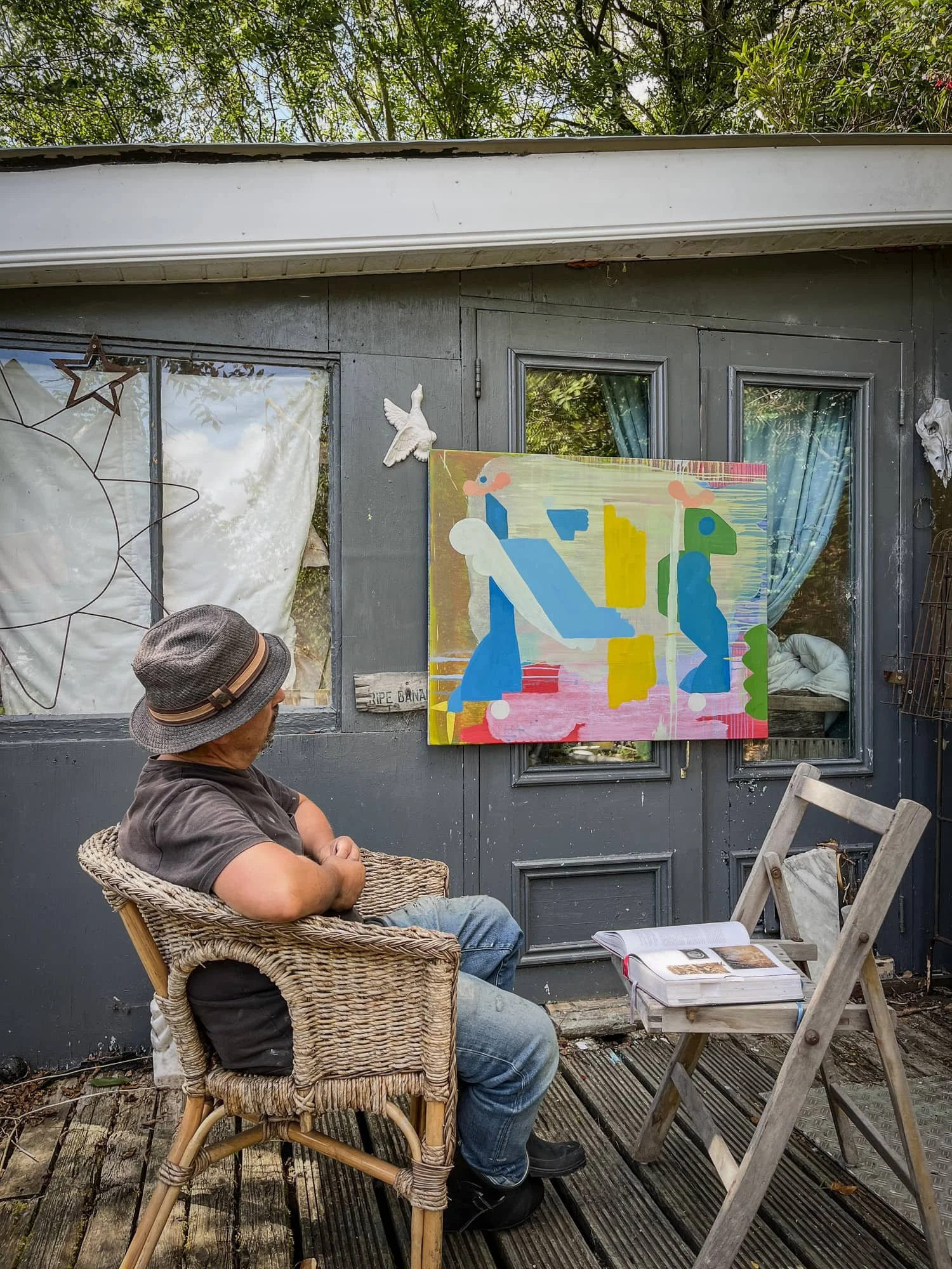 Irish artist seated outdoors studying colourful abstract oil painting propped against studio exterior, Martin Finnin
