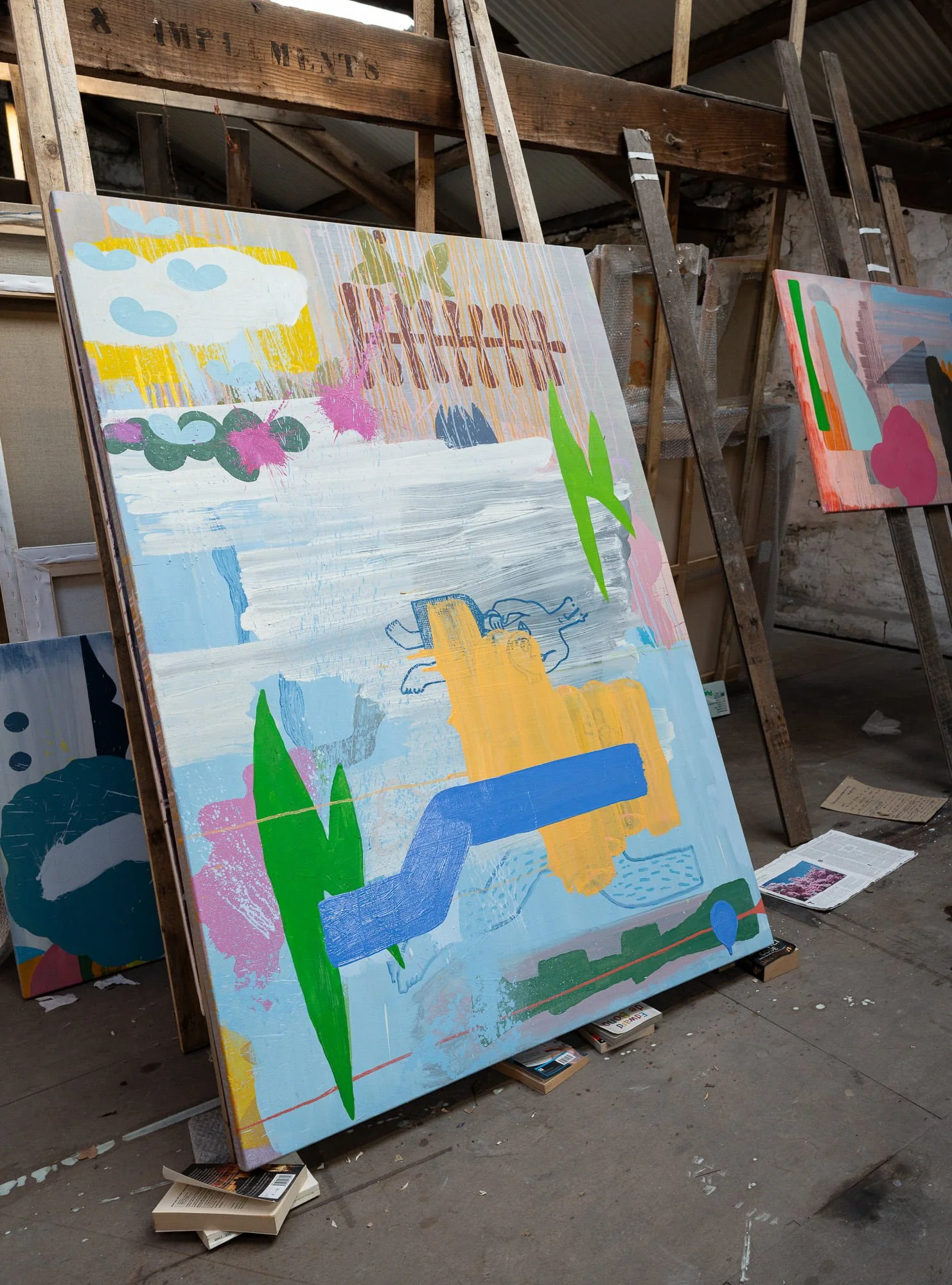 Large abstract oil painting leaning against easel in West Cork studio, pale blue ground with green yellow blue and pink forms developing, multiple canvases visible in background, Martin Finnin Irish artist