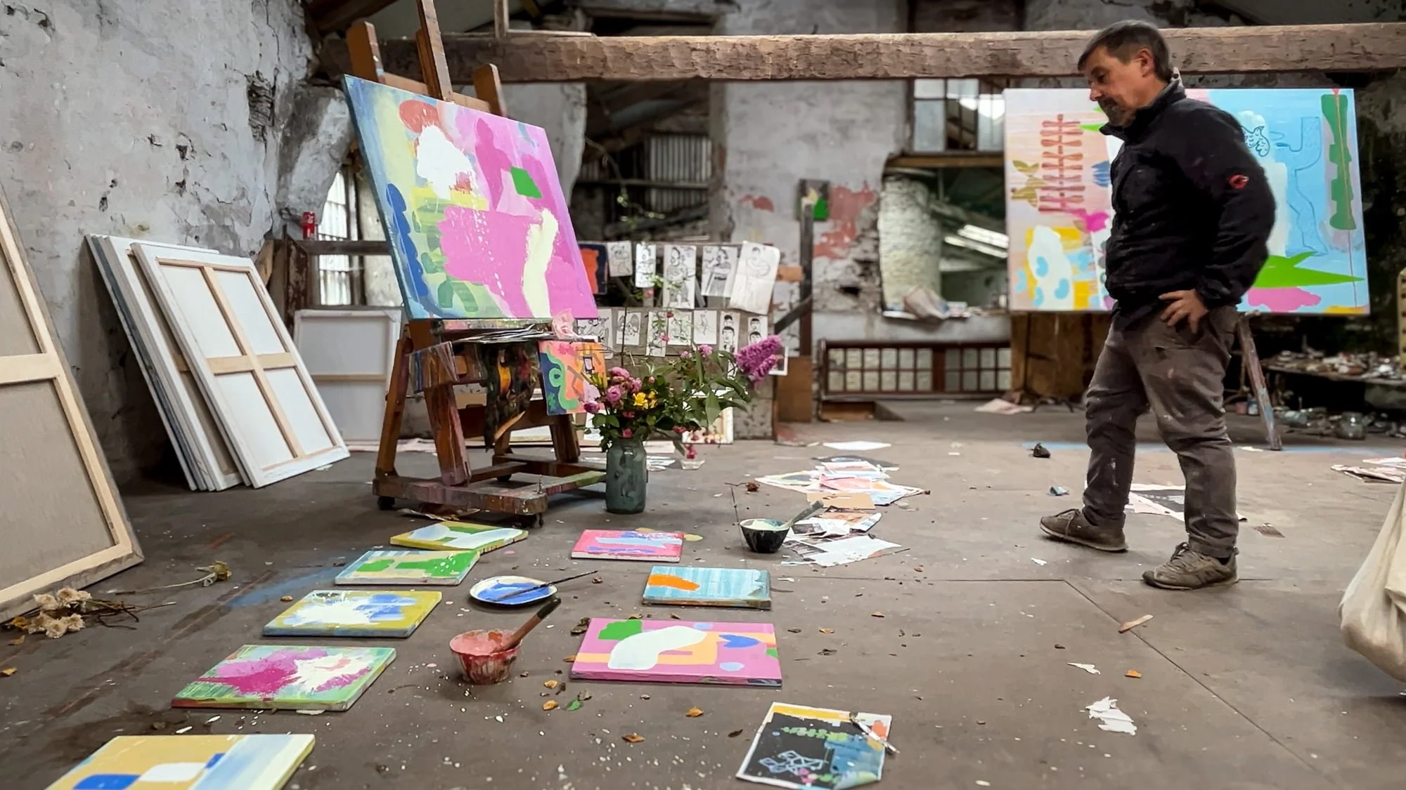 Irish artist surveying multiple small abstract oil paintings laid out on studio floor, large canvas on easel and two large works in background, West Cork studio, Martin Finnin