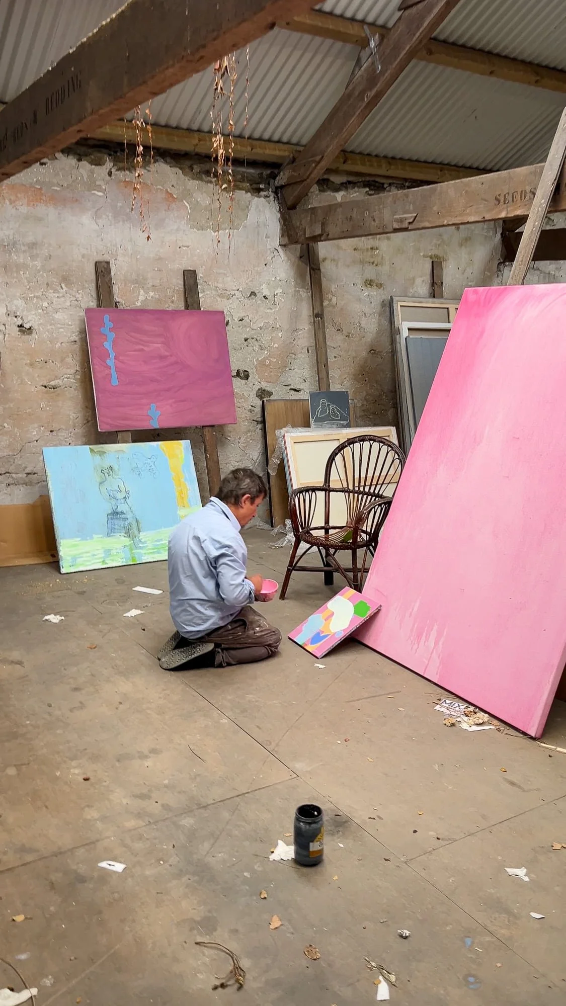 Irish artist Martin Finnin kneeling on studio floor surrounded by multiple canvases in early stages, large pink canvas and figurative works in progress in Cork studio