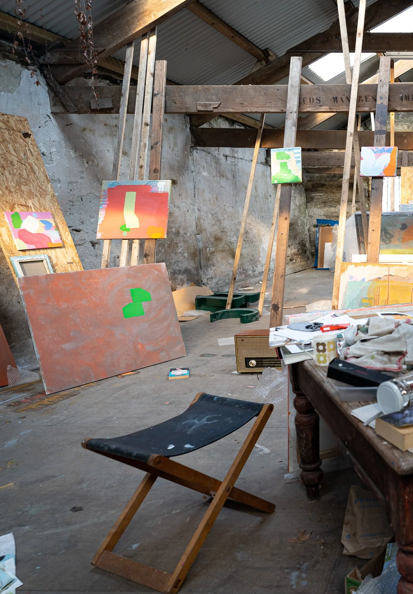 Early stage terracotta canvas with green forms among multiple paintings in large West Cork studio, working studio atmosphere with easels and found objects, Martin Finnin Irish artist