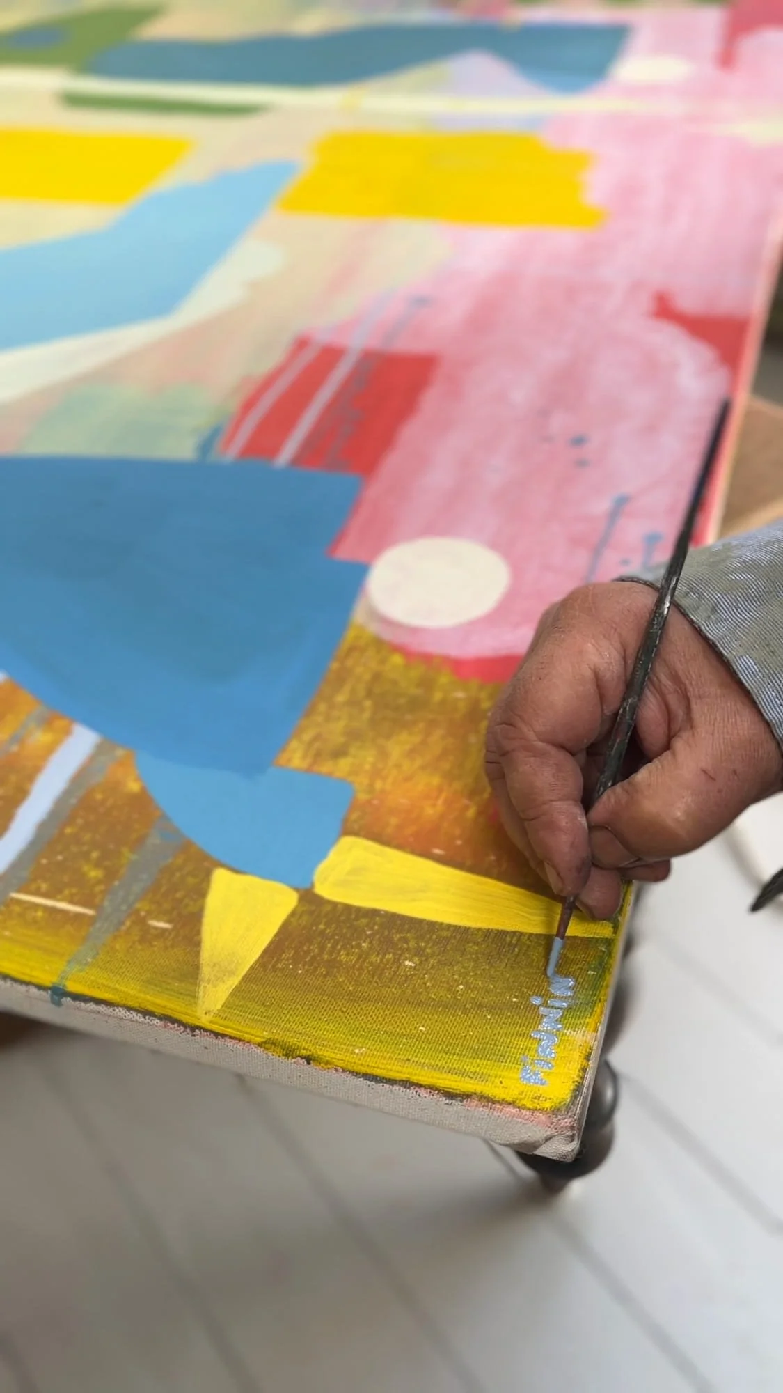 Artist's hand signing finished oil painting, blue yellow pink and red canvas edge showing paint depth, West Cork studio, Martin Finnin Irish artist