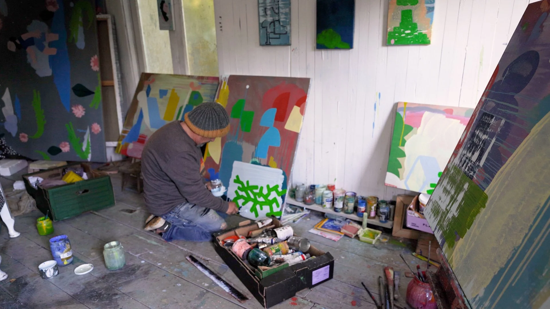 Irish artist working close to canvas on studio floor surrounded by multiple paintings in progress, blue green yellow and terracotta forms, West Cork studio, Martin Finnin