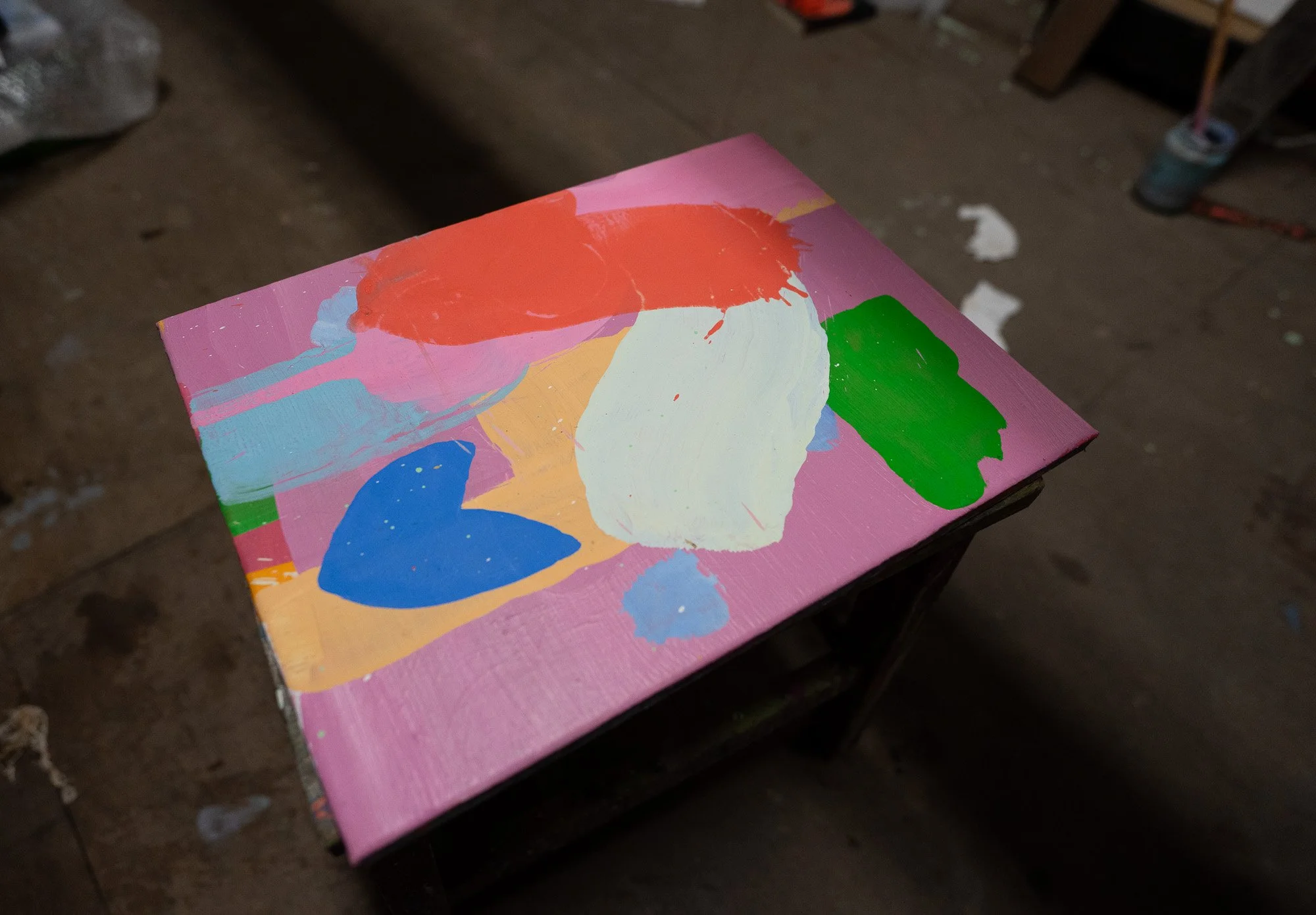 Small abstract oil painting flat on studio floor, vivid red white blue green and orange forms on pink ground, West Cork studio, Martin Finnin Irish artist
