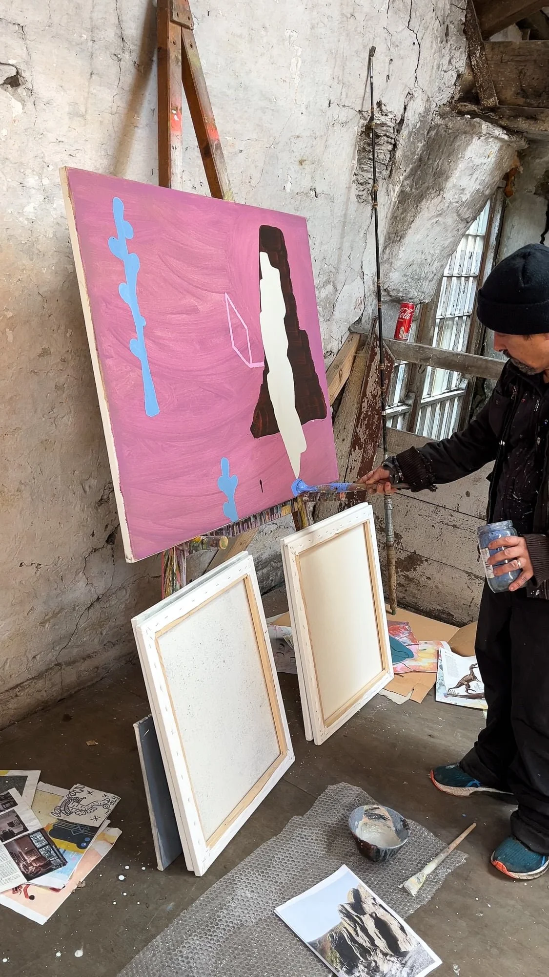 Irish artist Martin Finnin painting blue forms onto pink abstract canvas on easel in West Cork studio, early stage oil painting with dark brown and cream shapes emerging, painting in progress