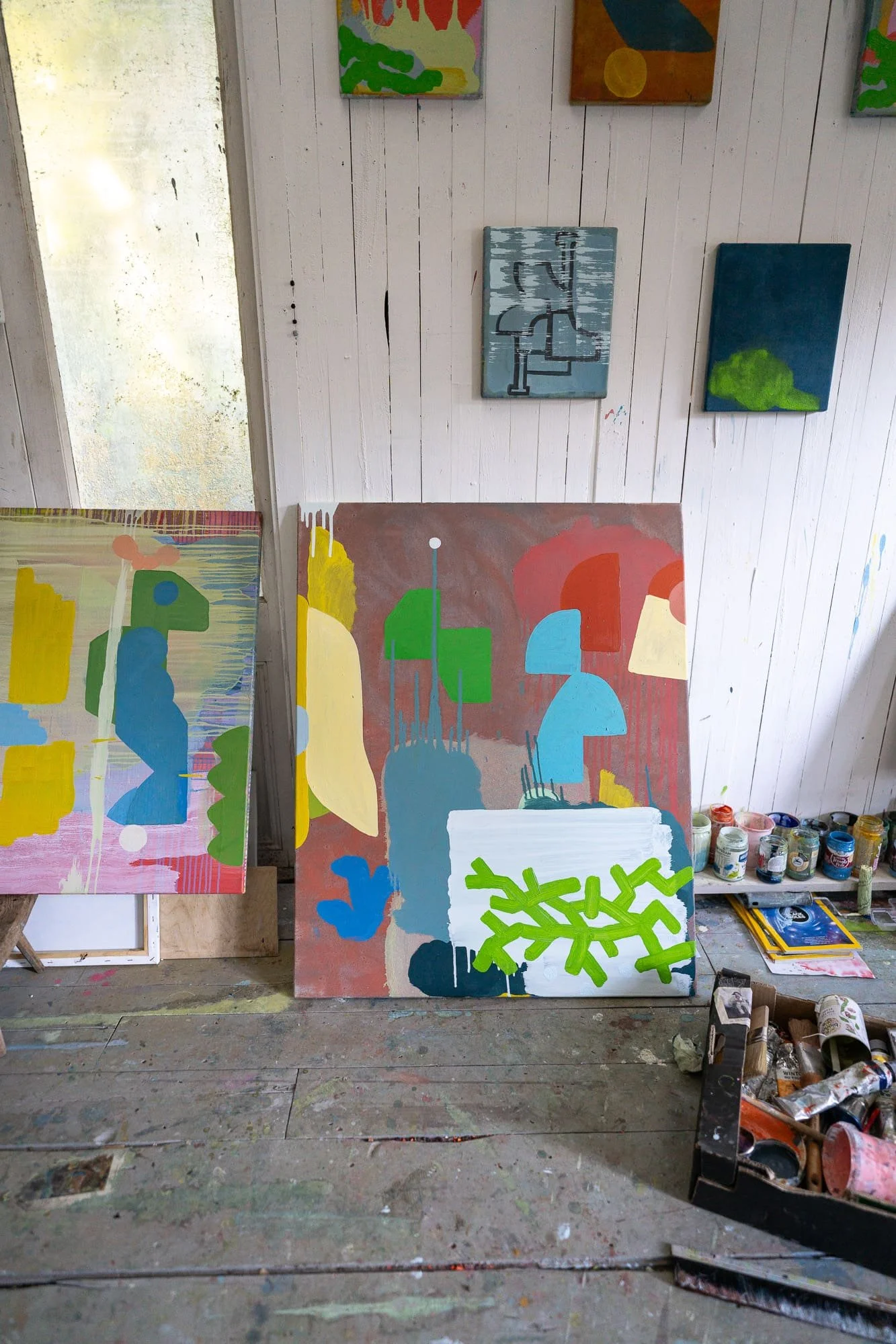 Two large abstract oil paintings in progress leaning against West Cork studio wall, terracotta green blue and yellow forms, smaller works pinned above, Martin Finnin Irish artist