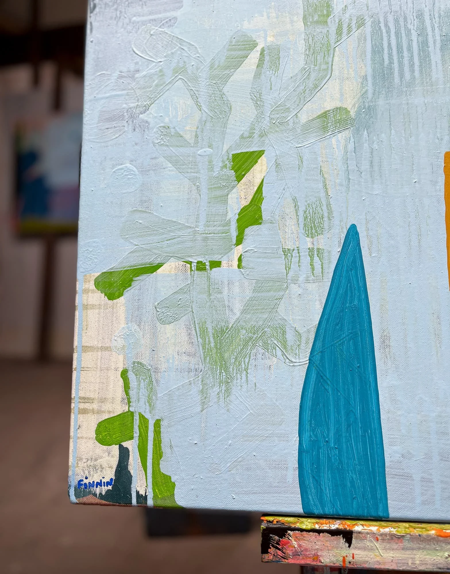Close up of canvas corner on easel showing pale blue ground with green botanical forms and teal blue shape, layered oil paint surface detail, Martin Finnin West Cork studio