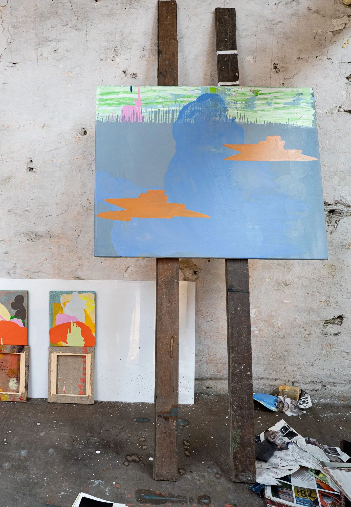 Abstract oil painting in progress on easel in West Cork studio, blue canvas with orange forms and mint green sky developing, smaller canvases visible alongside, Martin Finnin