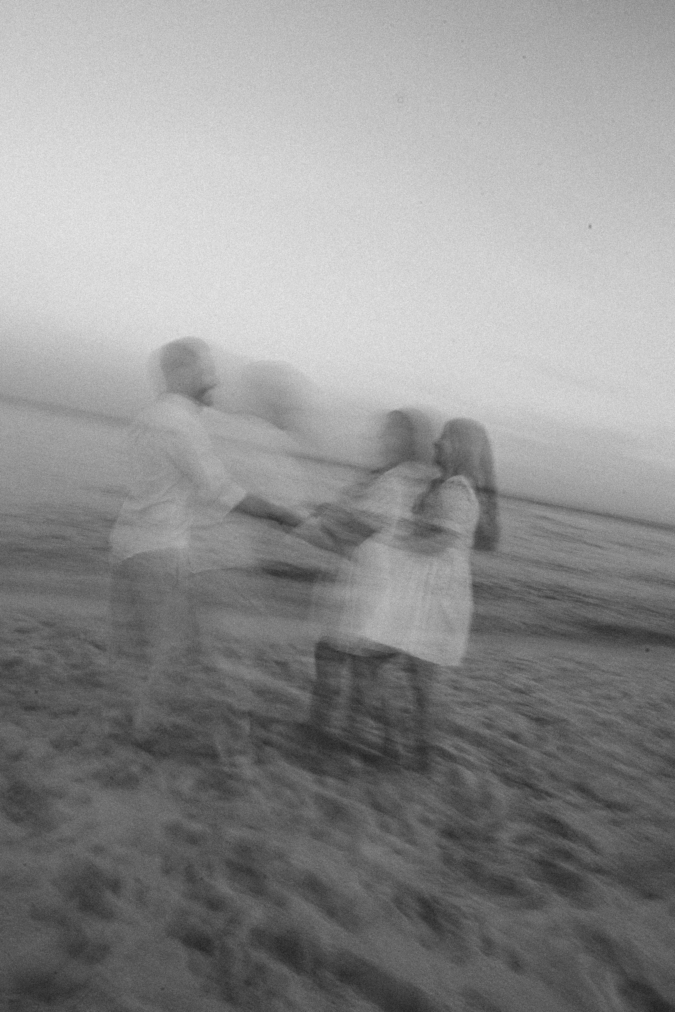 Two children standing on a beach at sunset, holding hands and playing together, with the ocean in the background.