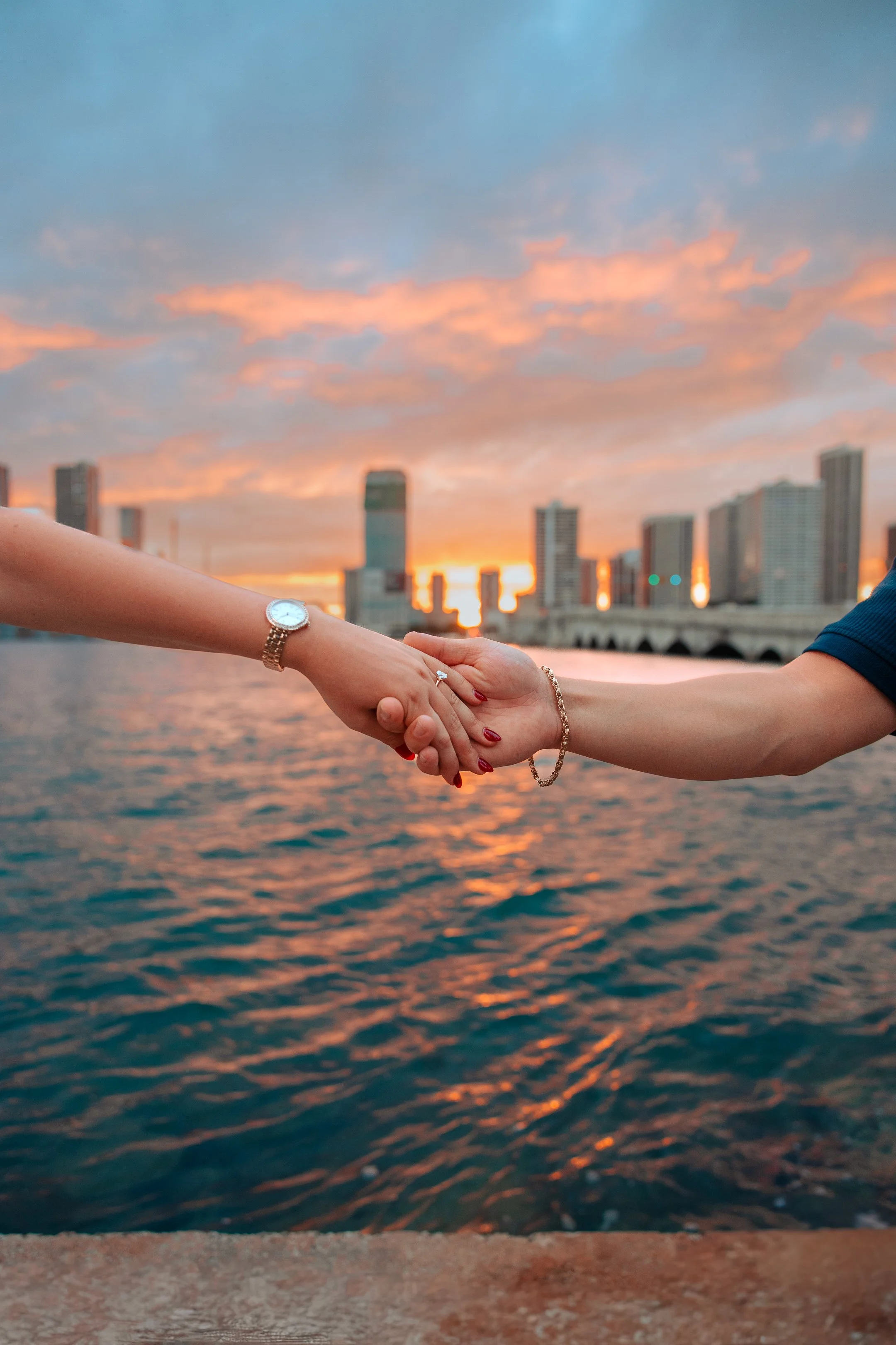 Two people shaking hands over water with a city skyline and sunset in the background.
