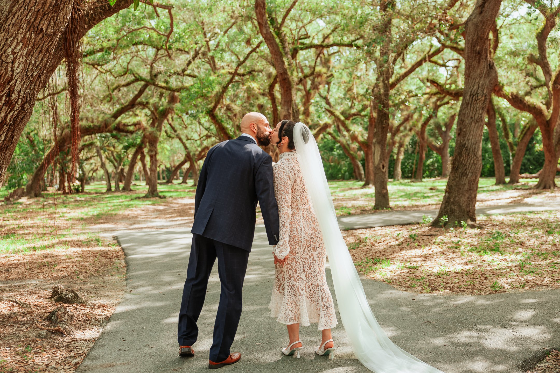 Bride and groom sharing a kiss on a wooded pathway during their wedding.
