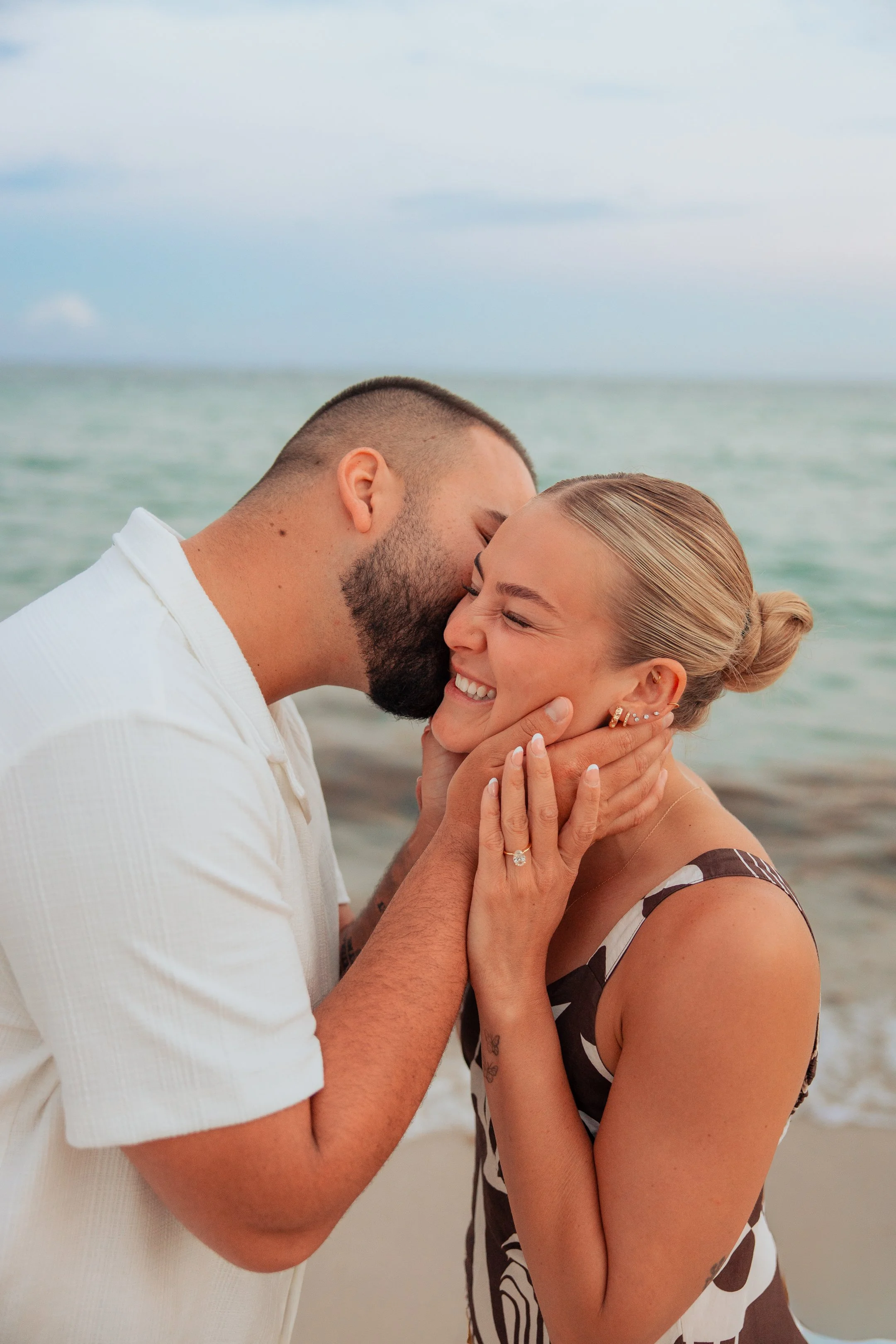 A couple embraces and shares a kiss on the beach with the ocean in the background.