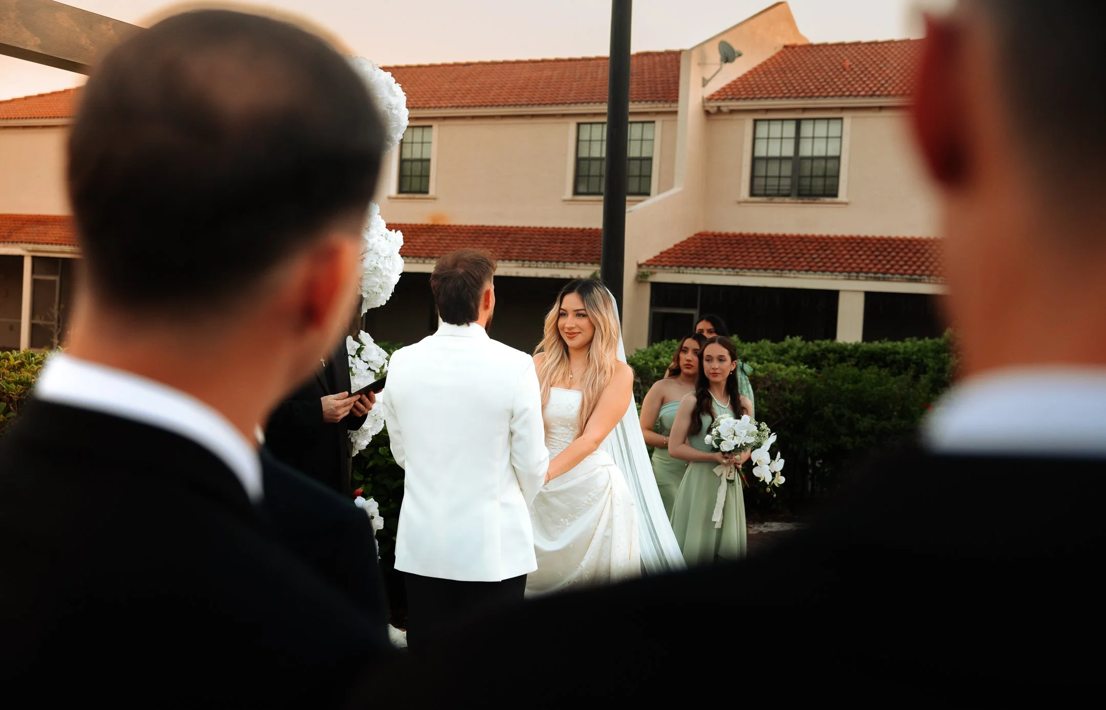 Wedding ceremony with the bride and groom holding hands, surrounded by bridesmaids and groomsmen outdoors.