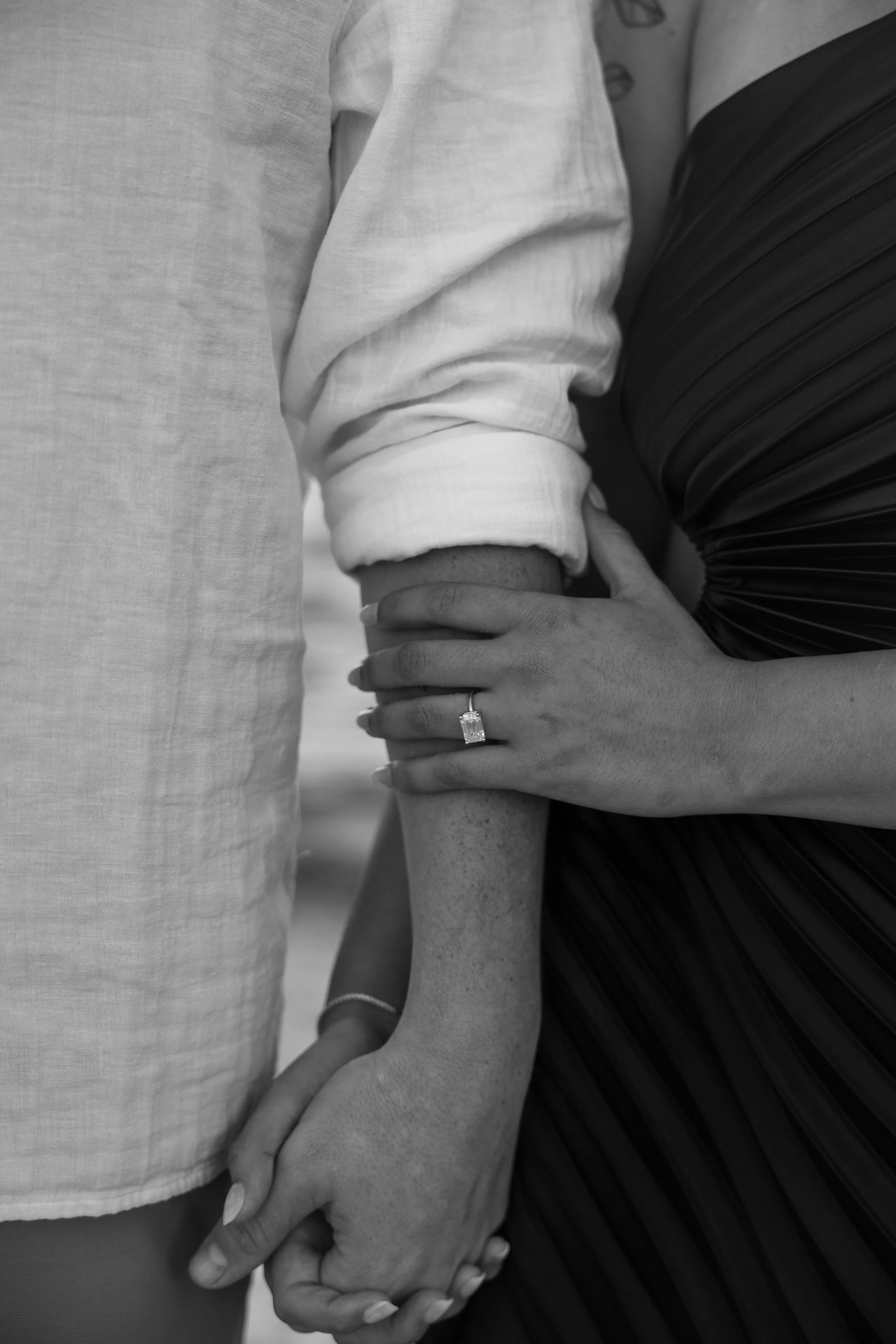 A black and white photo of a couple holding hands, with the woman wearing an engagement ring on her finger.