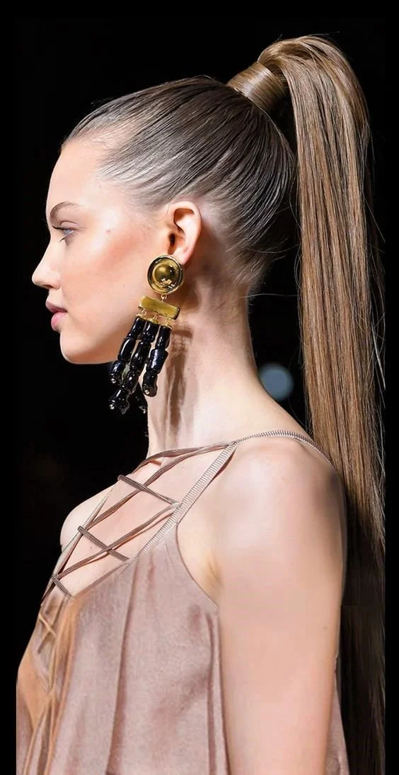 Profile of woman with sleek high ponytail, wearing large statement earrings and a strappy top.
