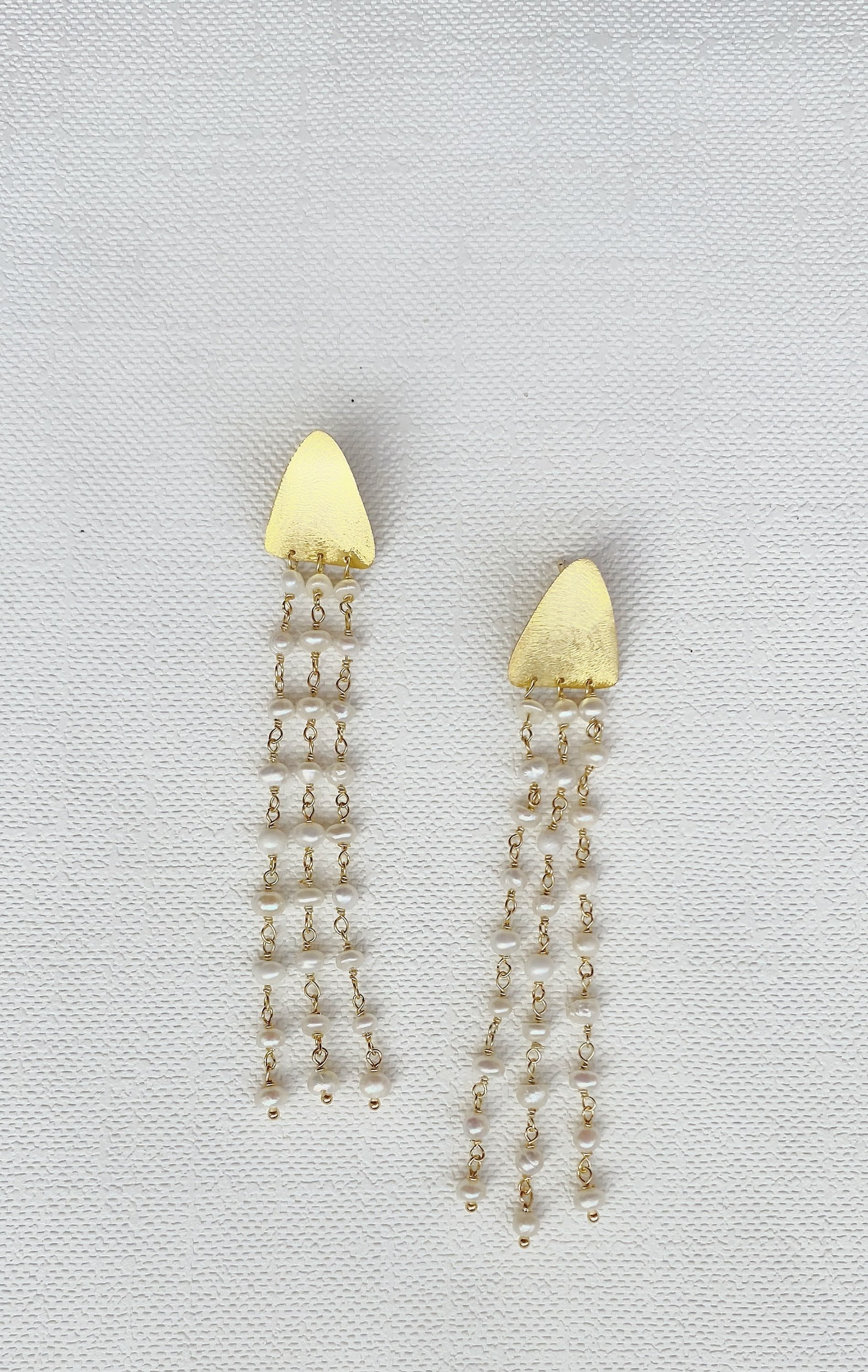 Gold triangle earrings with pearl strands on white background