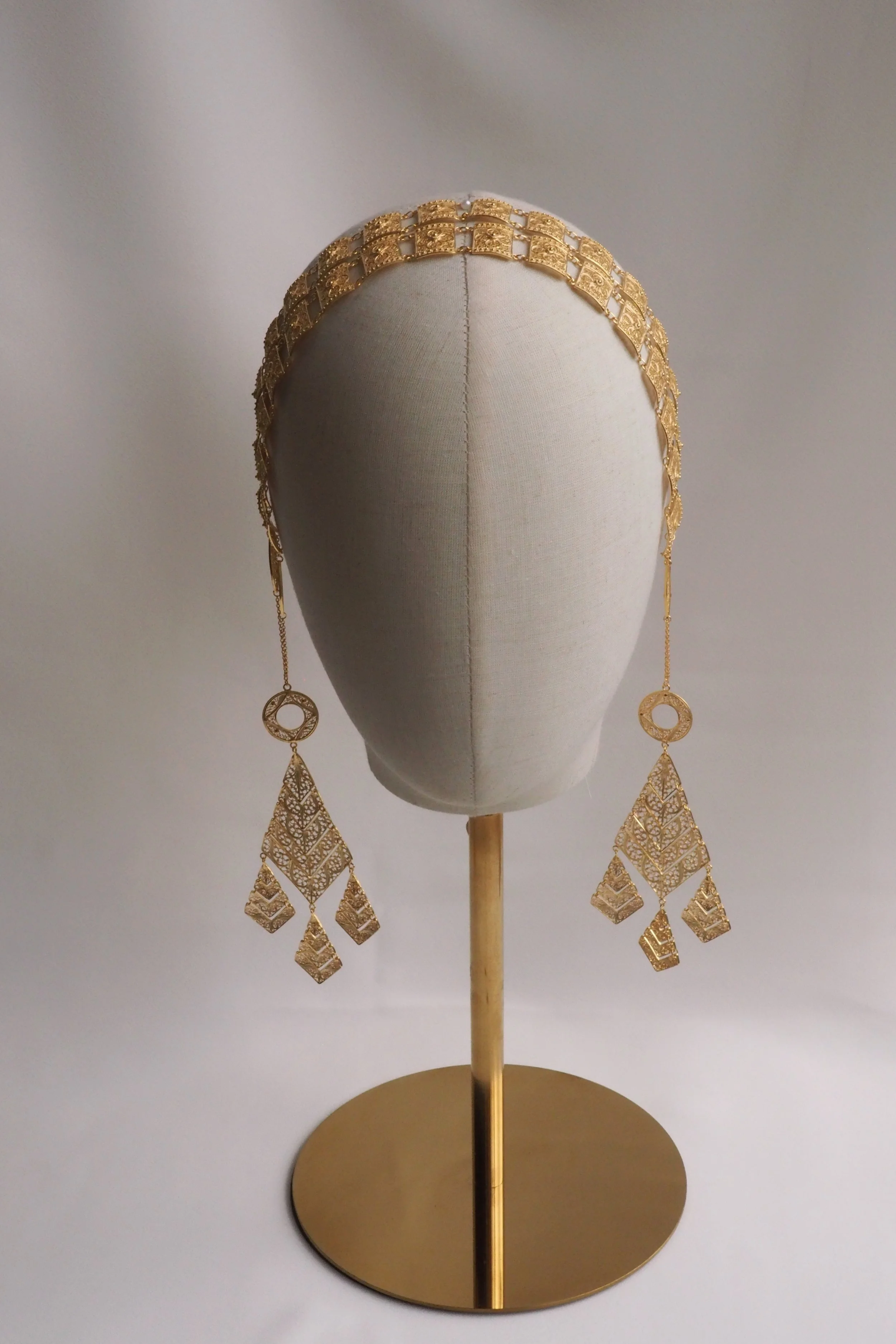 Gold decorative headpiece on mannequin head with geometric designs.