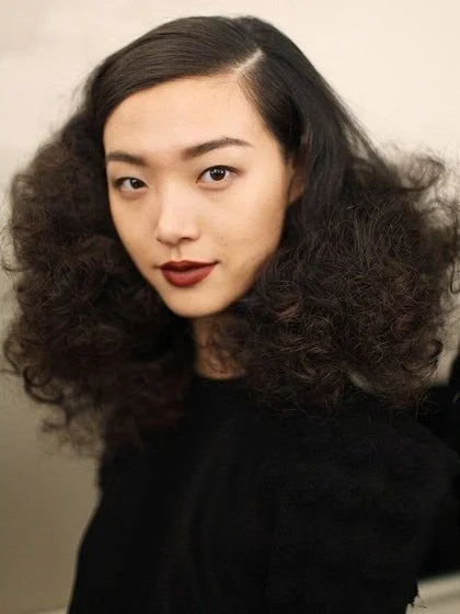Woman with voluminous curly hair and red lipstick wearing a black top.