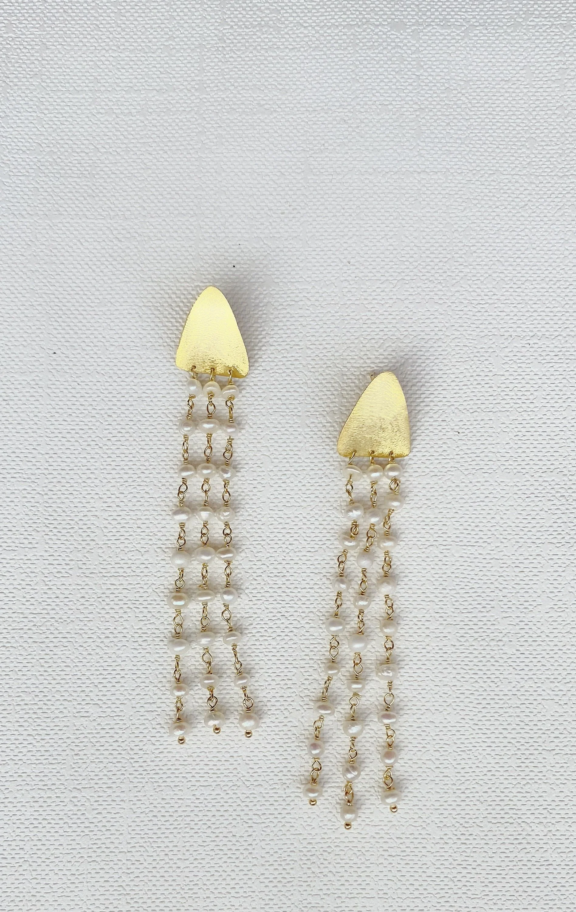Gold triangular stud earrings with dangling pearl chains on a white background.
