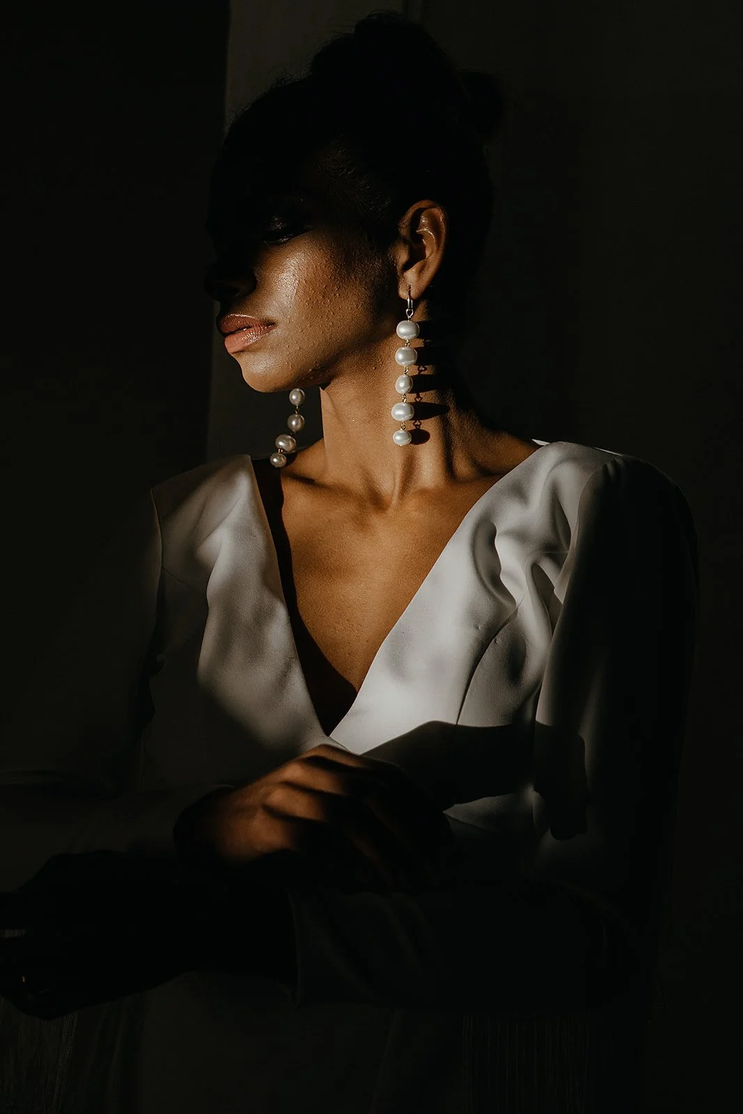 Woman in a white dress with pearl earrings, partially in shadow, with a contemplative pose.