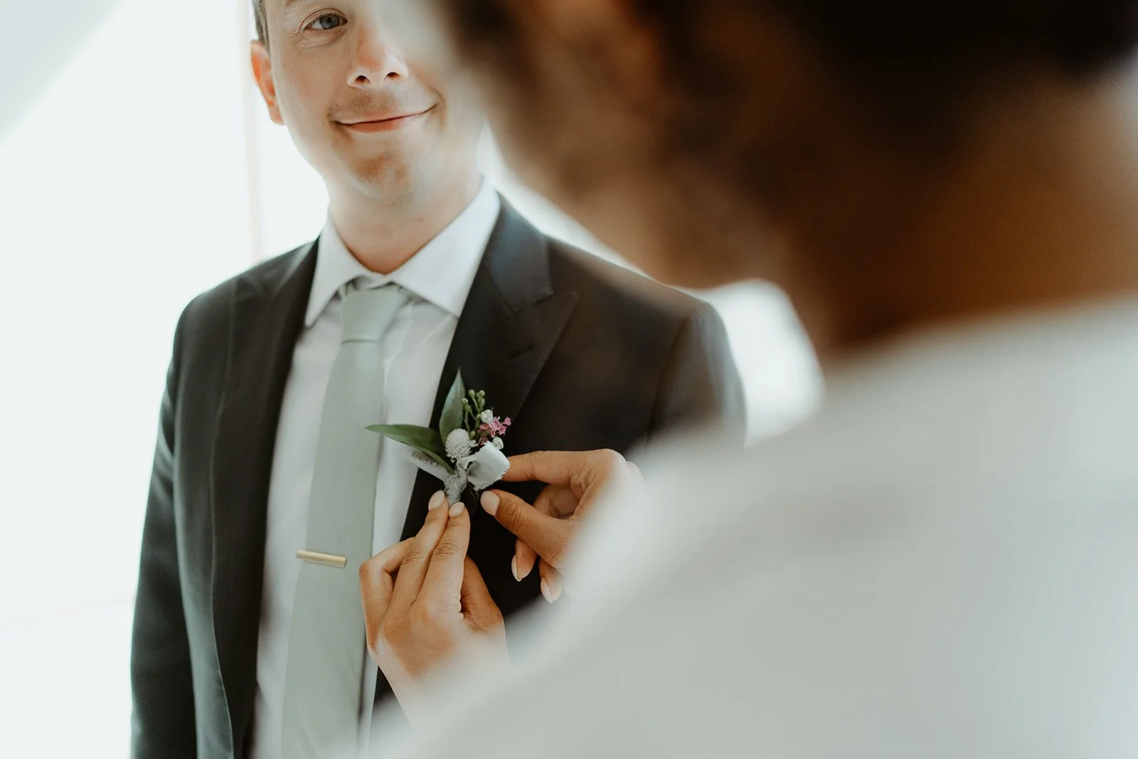 Person in a suit with a boutonniere being adjusted by someone else