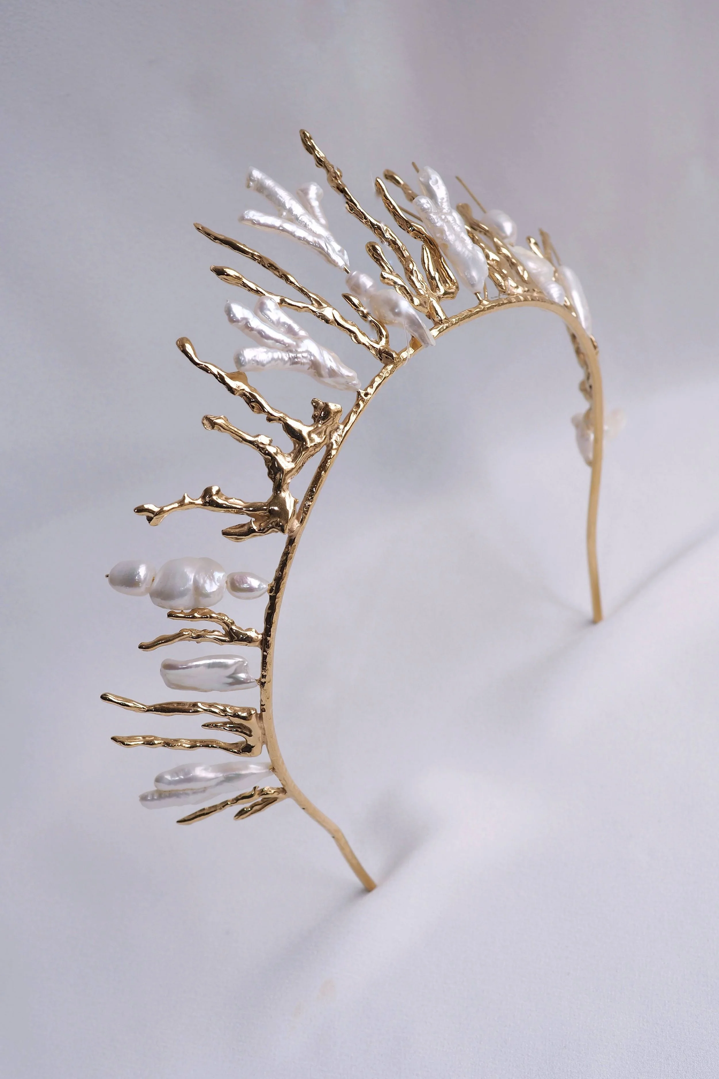 Gold tiara with white pearl accents on light background.
