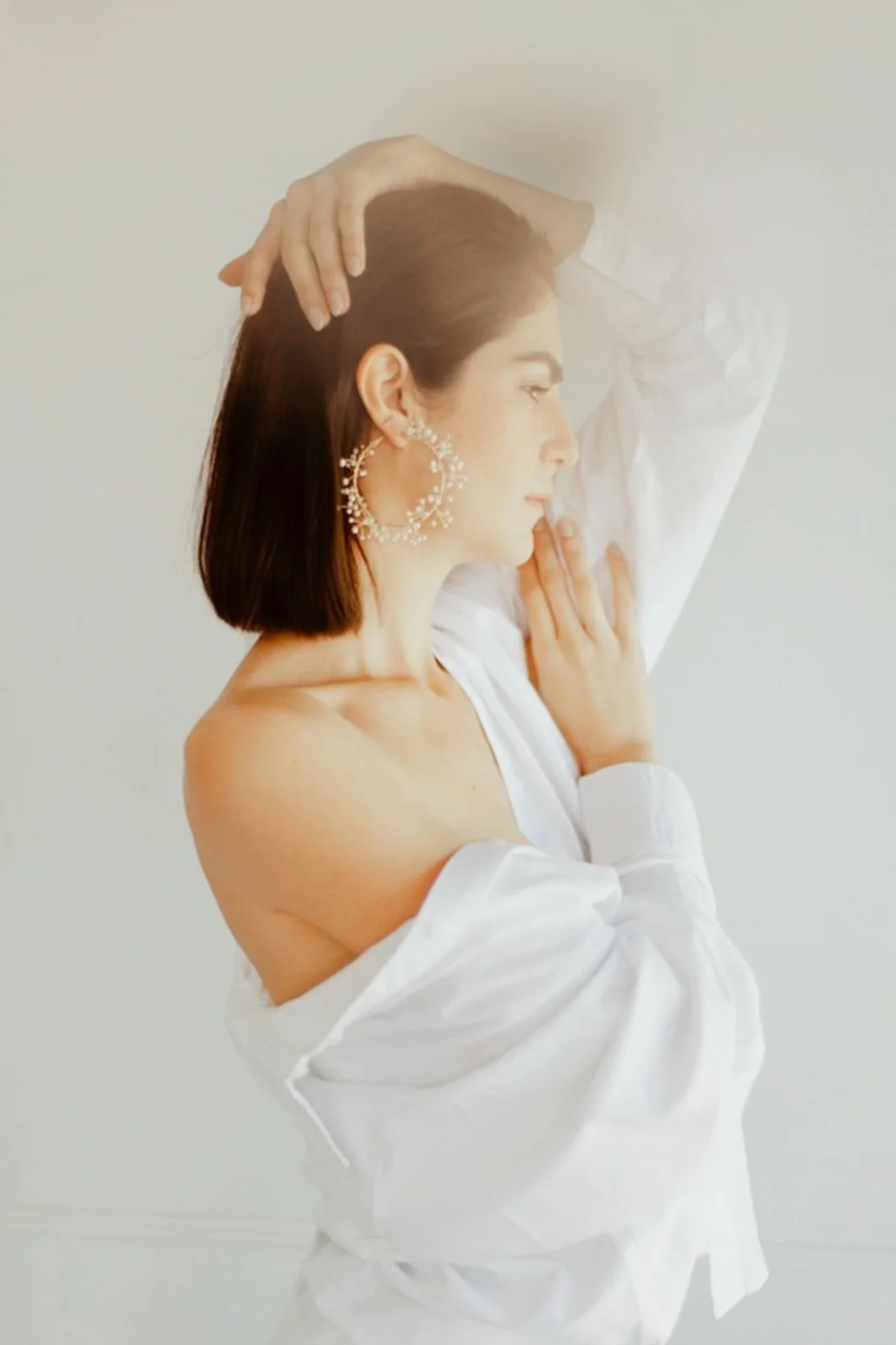 Woman wearing a white shirt and large circular earrings, posing with arms raised.