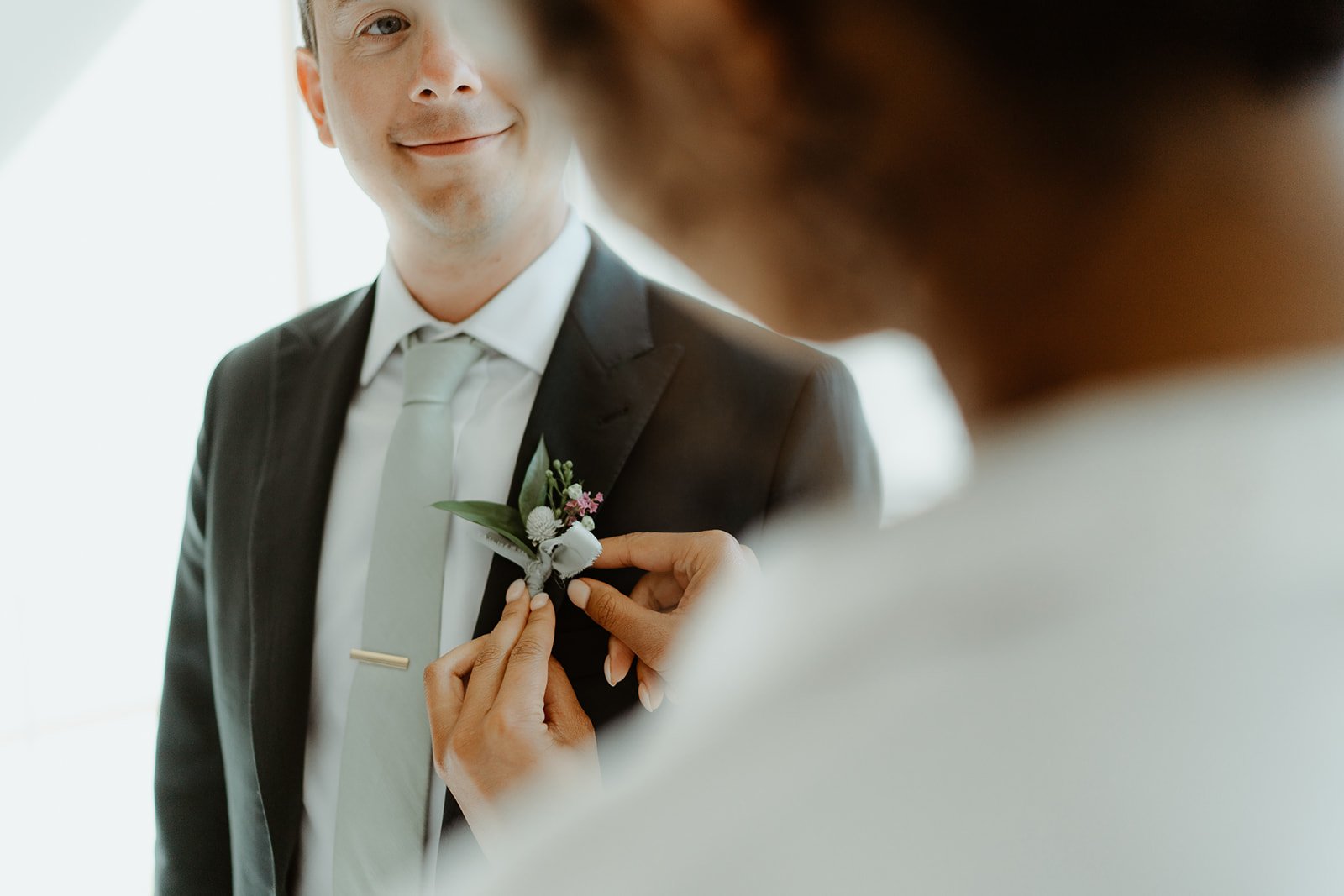 Person in a suit with a boutonniere being adjusted by someone else.