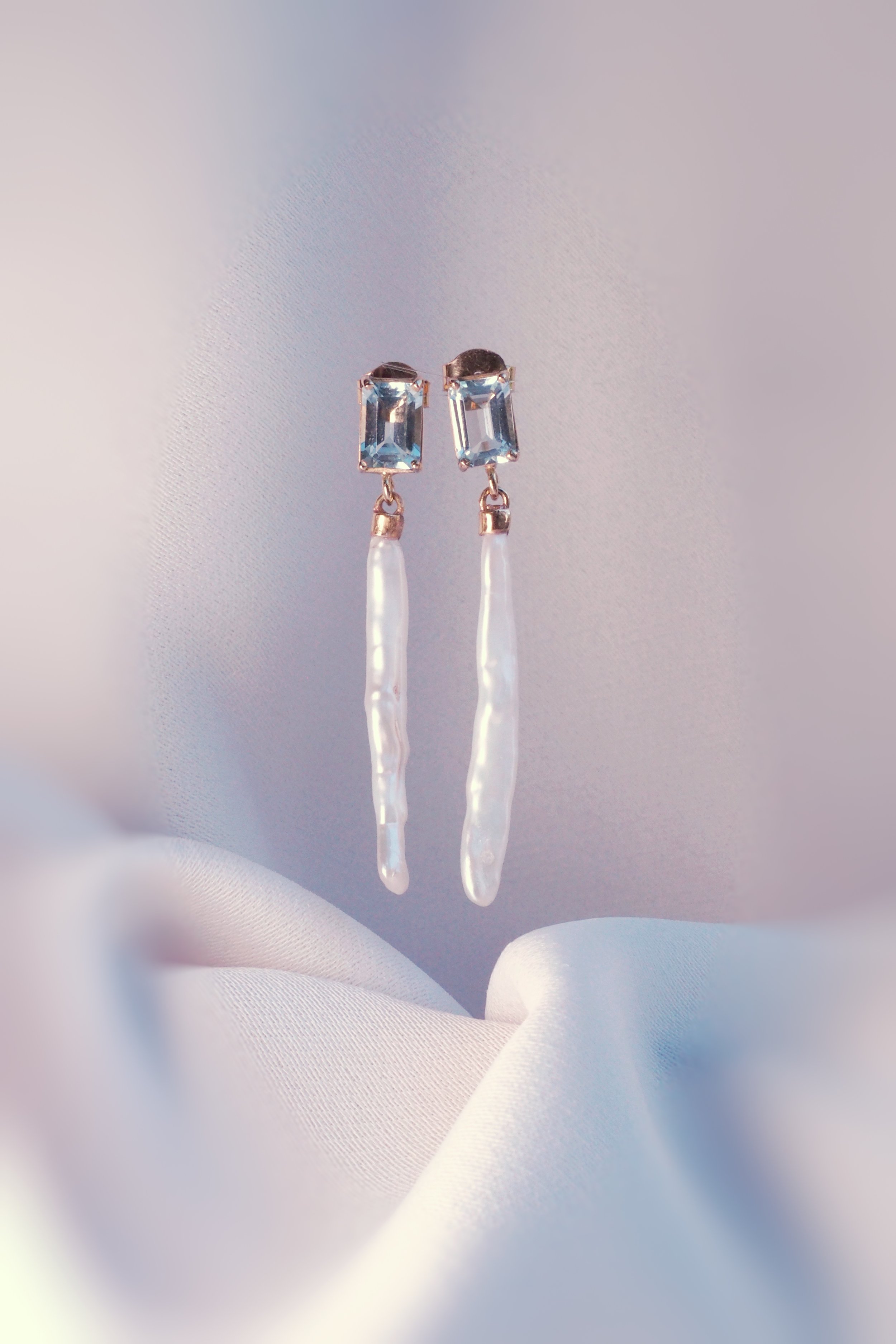 Dangling pearl earrings with blue gemstones on soft fabric background.