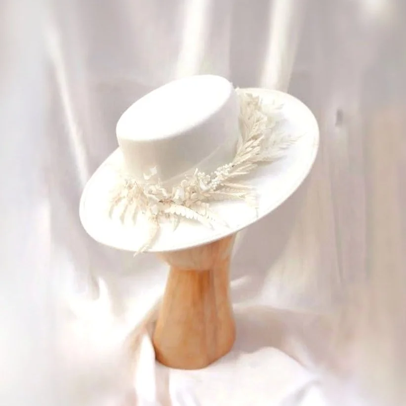 Elegant white hat with decorative flowers and feathers on a wooden stand
