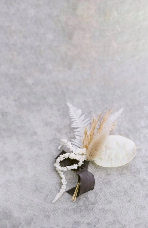 Minimalist floral boutonniere with dried flowers and black ribbon on light background.