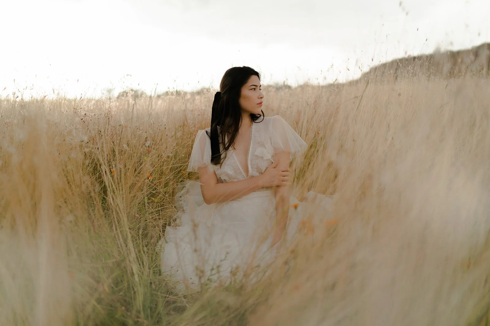 Woman in white dress sitting in tall grass field