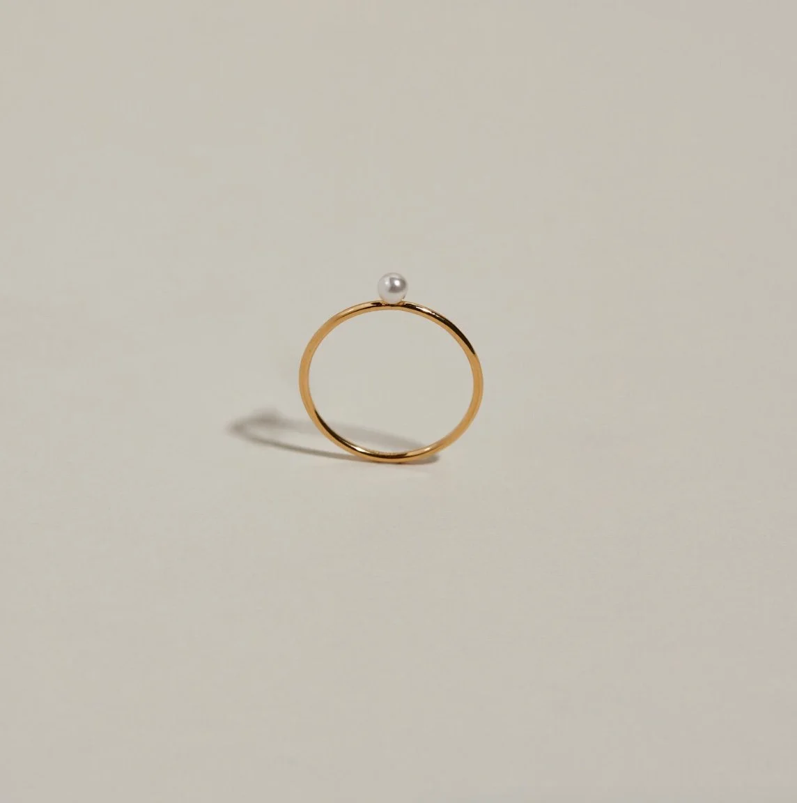 Minimalist gold ring with a small pearl accent on a light background.