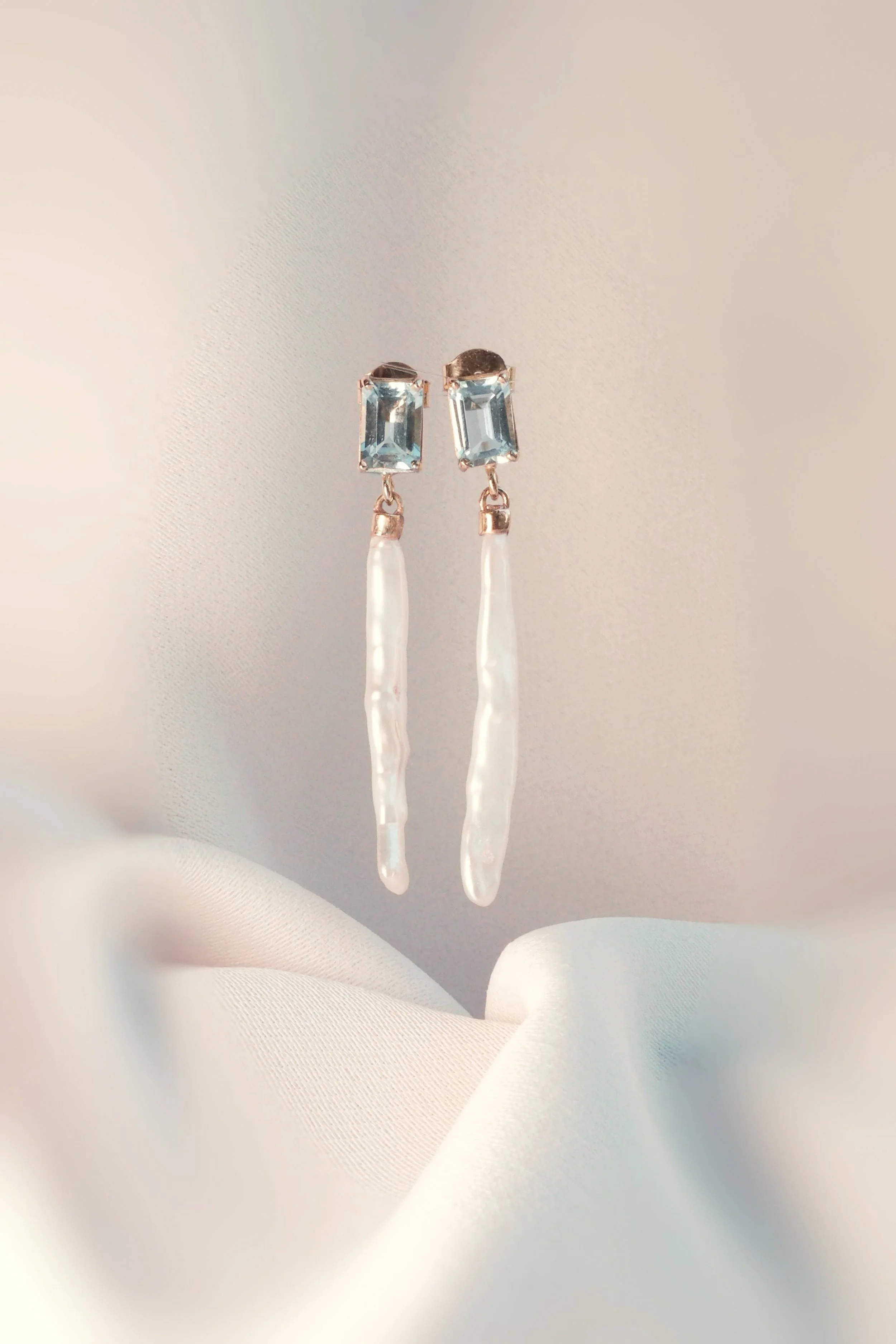 Earrings with blue gemstones and dangling pearls on white fabric background.