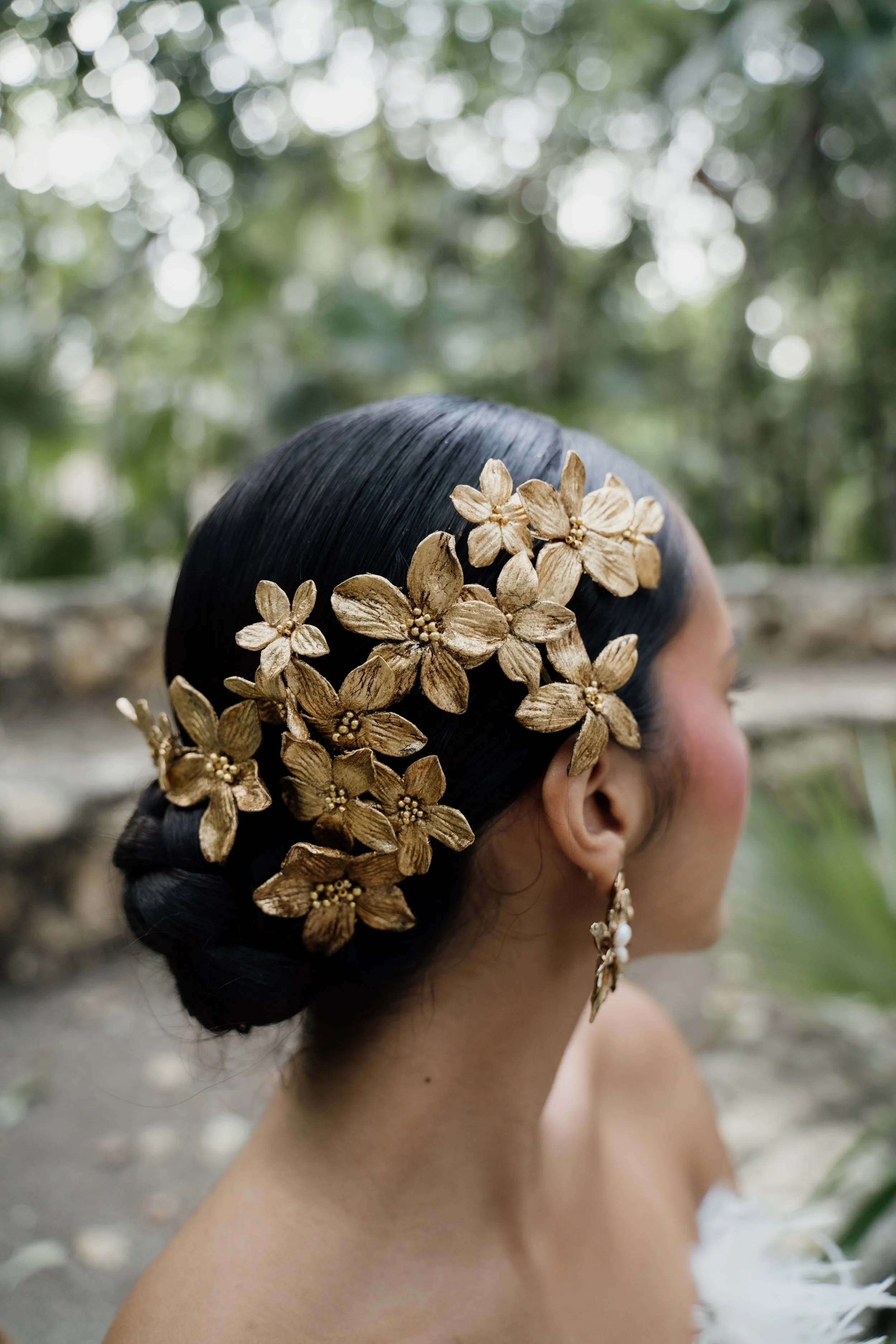 Woman with dark hair adorned with gold floral hair accessories, outdoor background.