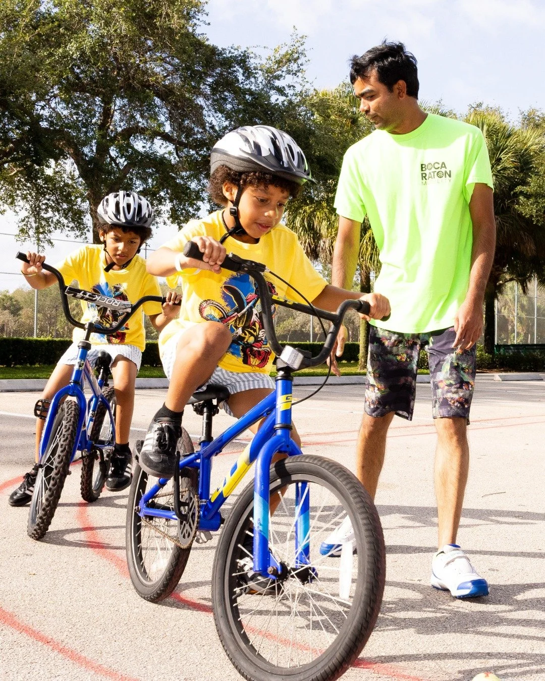 two young children learning to ride bicycles with an adult supervising