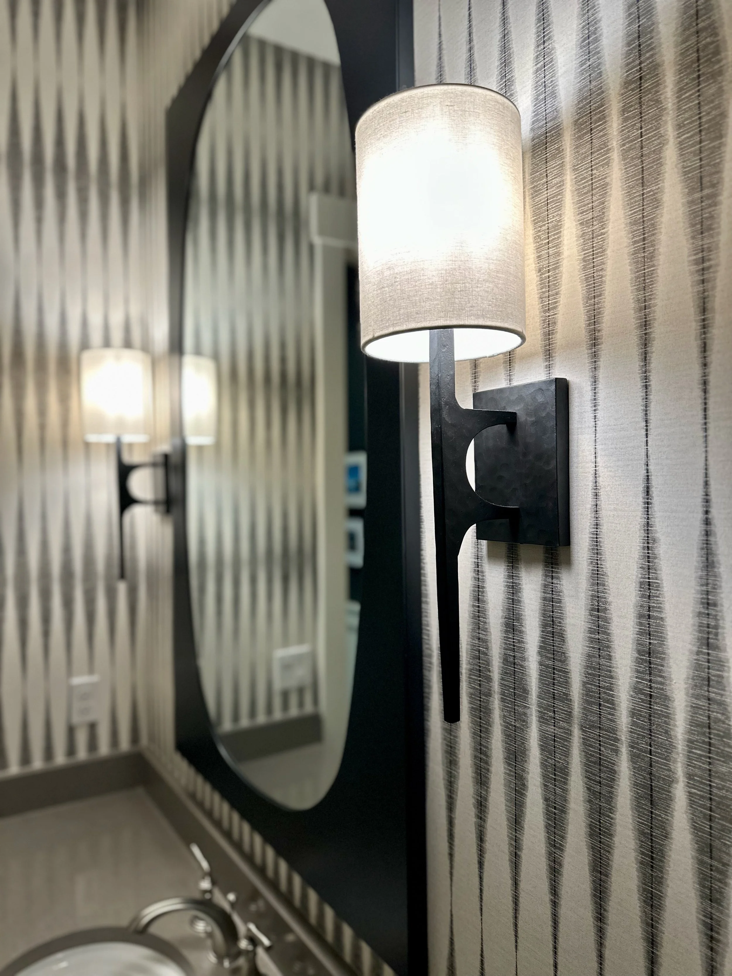 Modern bathroom with wall sconce, mirror, and patterned wallpaper.
