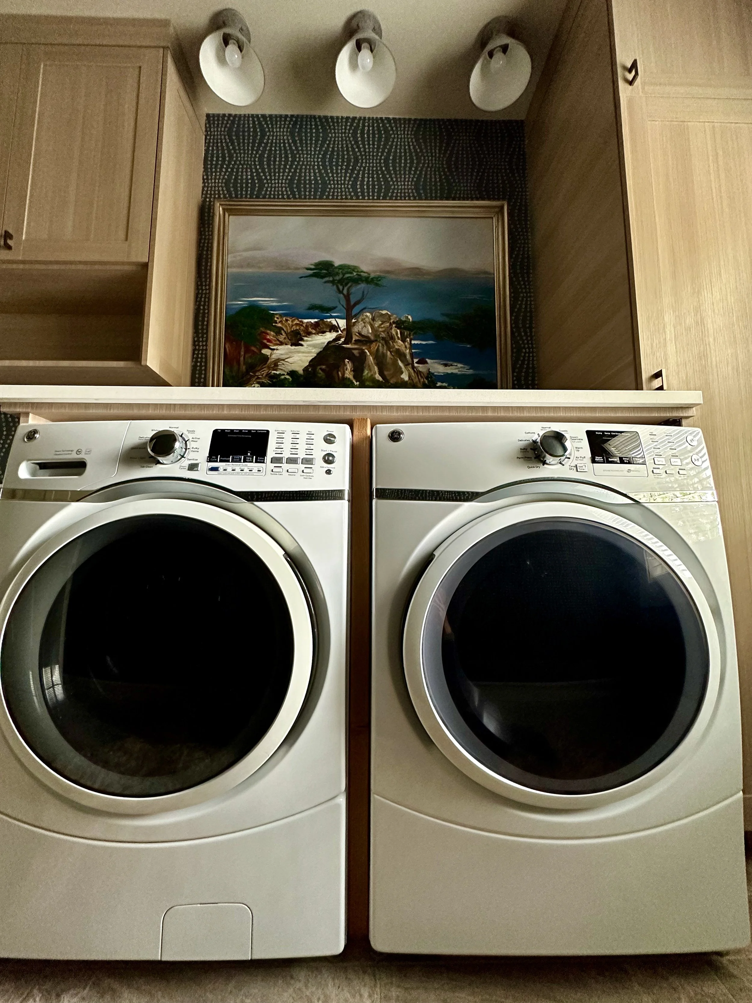 Laundry room with a front-load washer and dryer, cabinets, artwork, and ceiling lights.