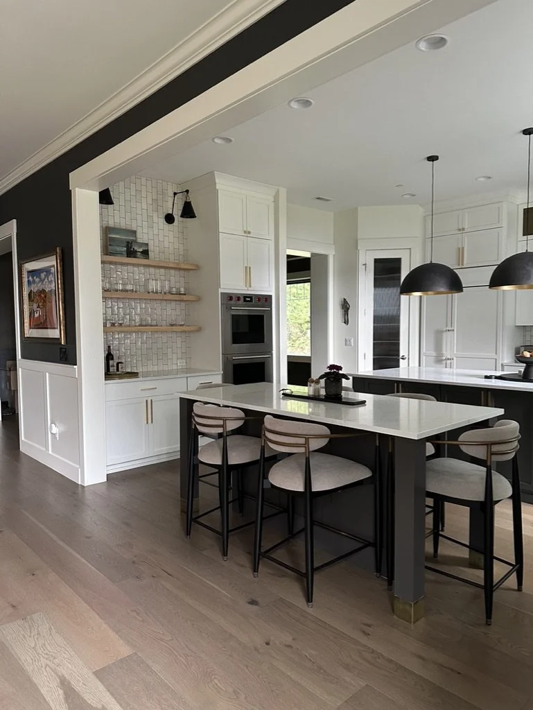 Modern kitchen with white cabinets, a large island with bar stools, pendant lights, open shelving, and wood flooring.