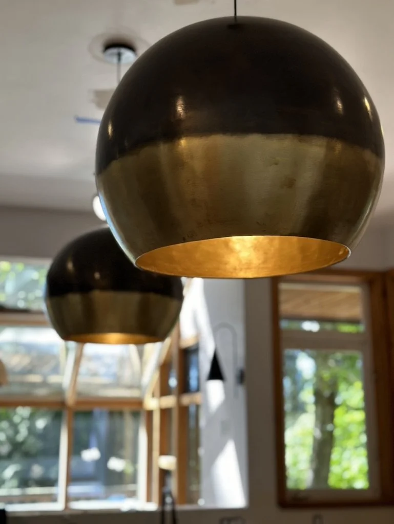Modern ceiling light fixtures with a gold finish in a bright room with large windows and natural light.