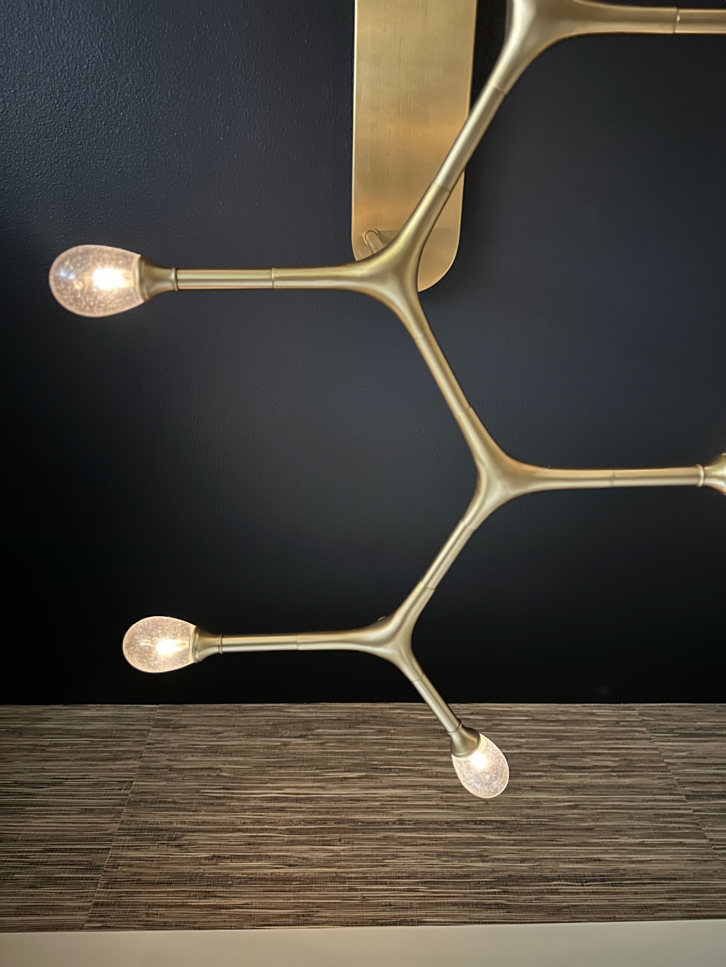 Modern gold-colored branched light fixture with three lit bulbs against a dark background.