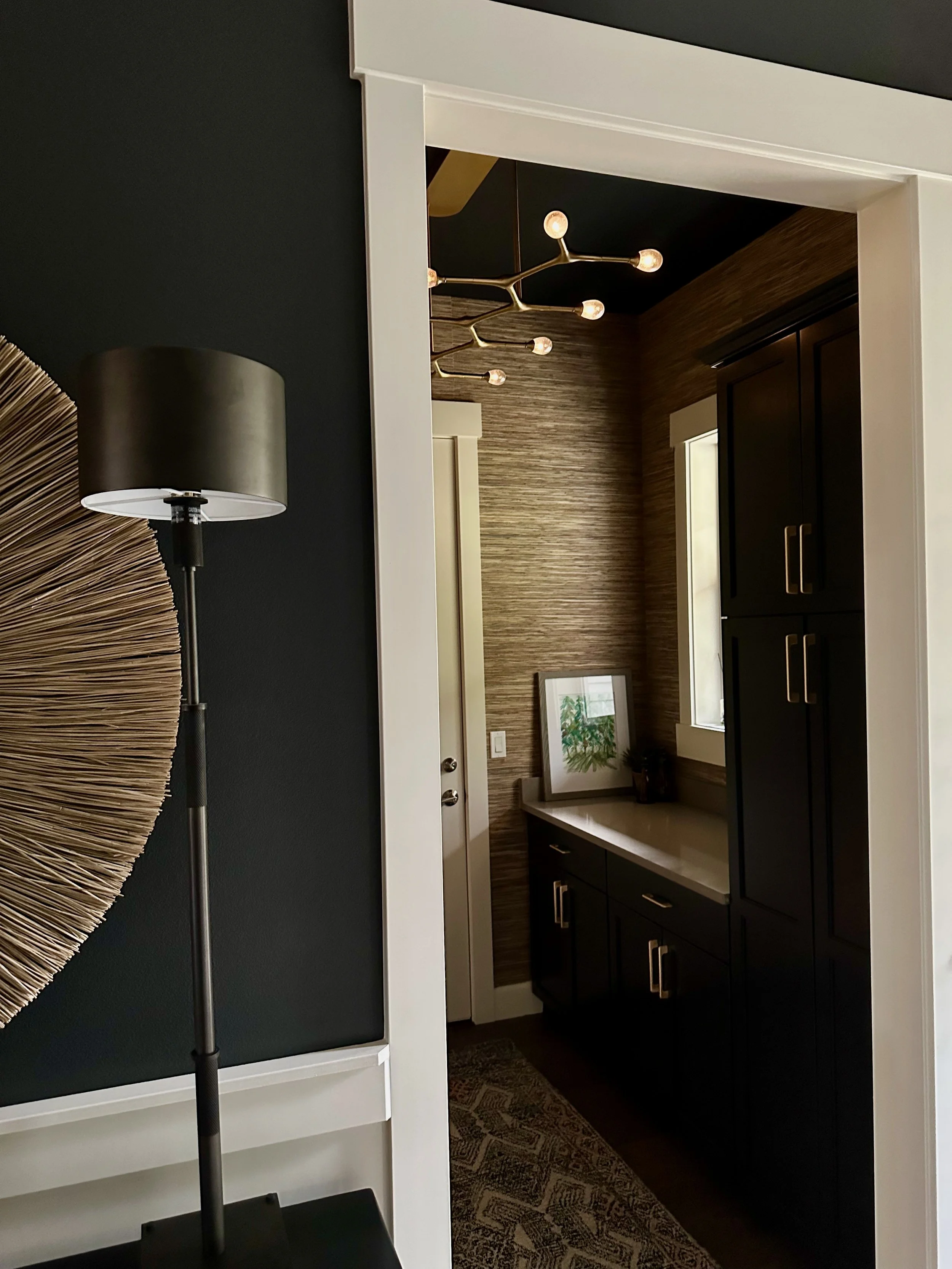 Modern interior hallway with black cabinetry, artistic light fixture, textured wall, decorative artwork, and floor lamp.