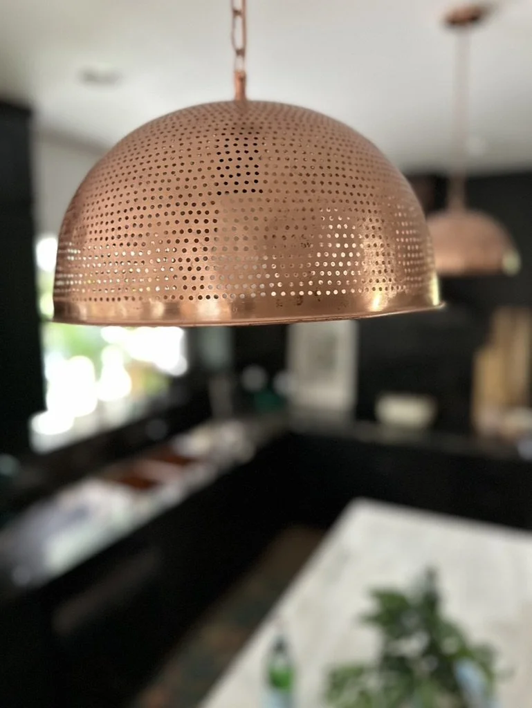 Copper perforated pendant light hanging in a modern kitchen with a marble countertop and blurred background.
