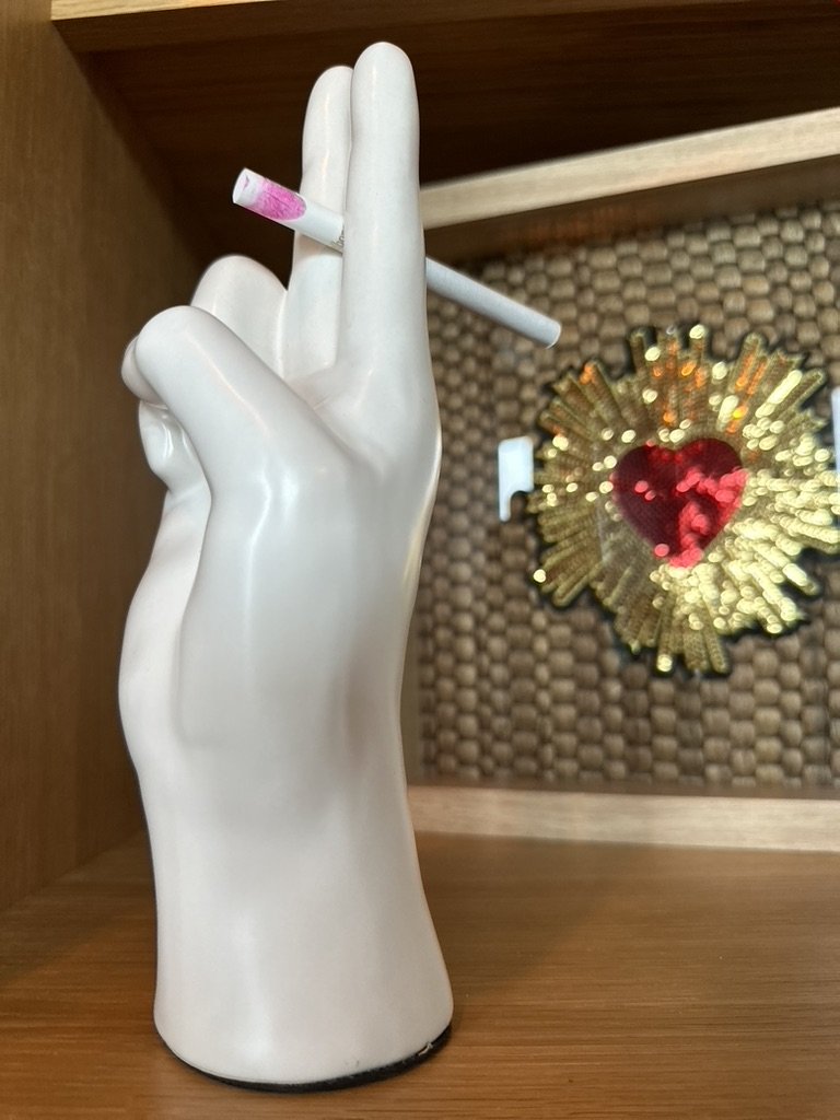 Ceramic hand statue holding a cigarette with pink lipstick mark, decorative heart in background.