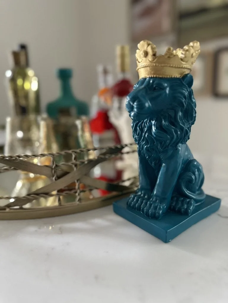 Teal lion statue wearing gold crown, near decorative bottle collection.