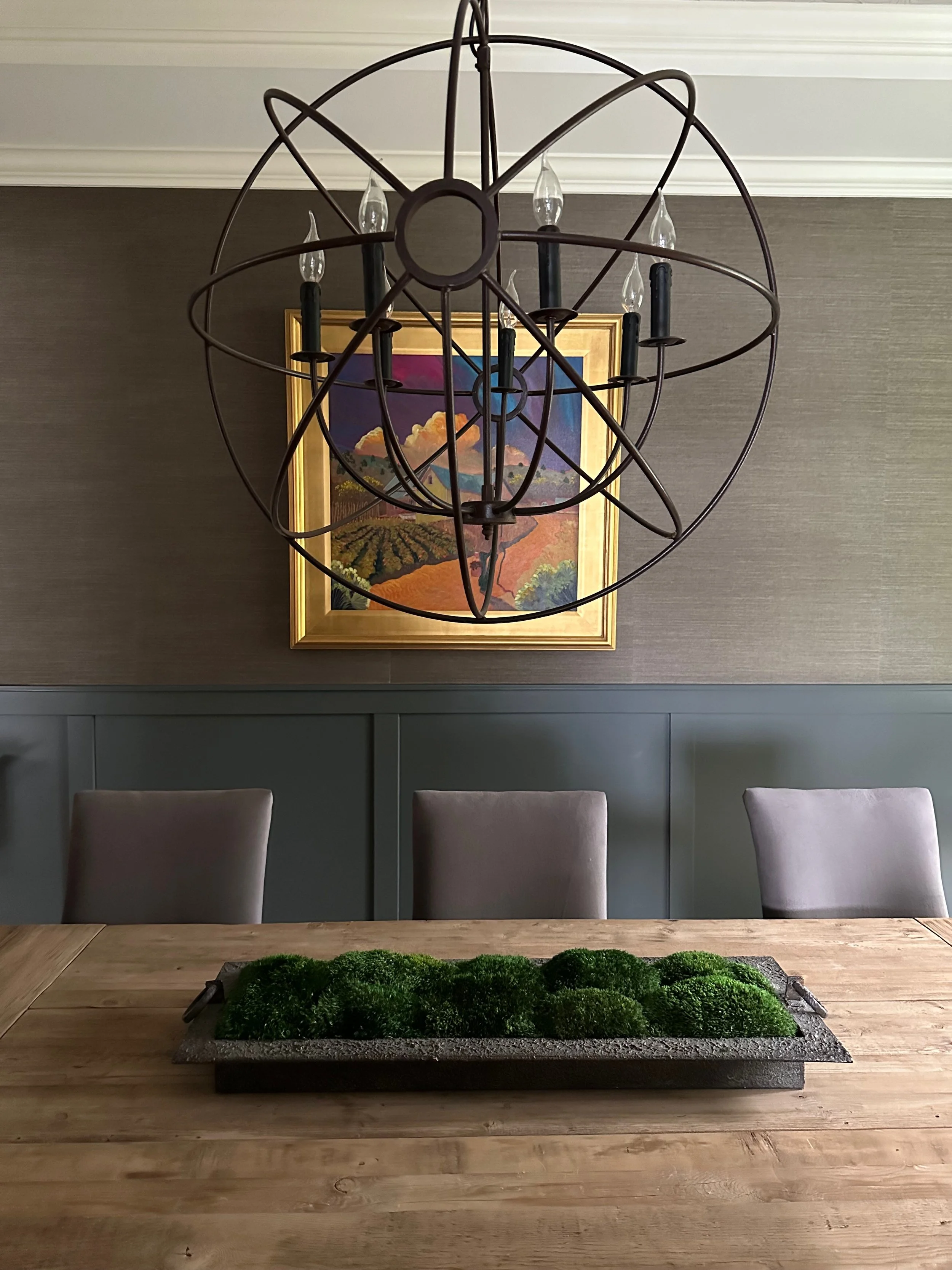 Dining room with modern chandelier, painting, table, and green centerpiece